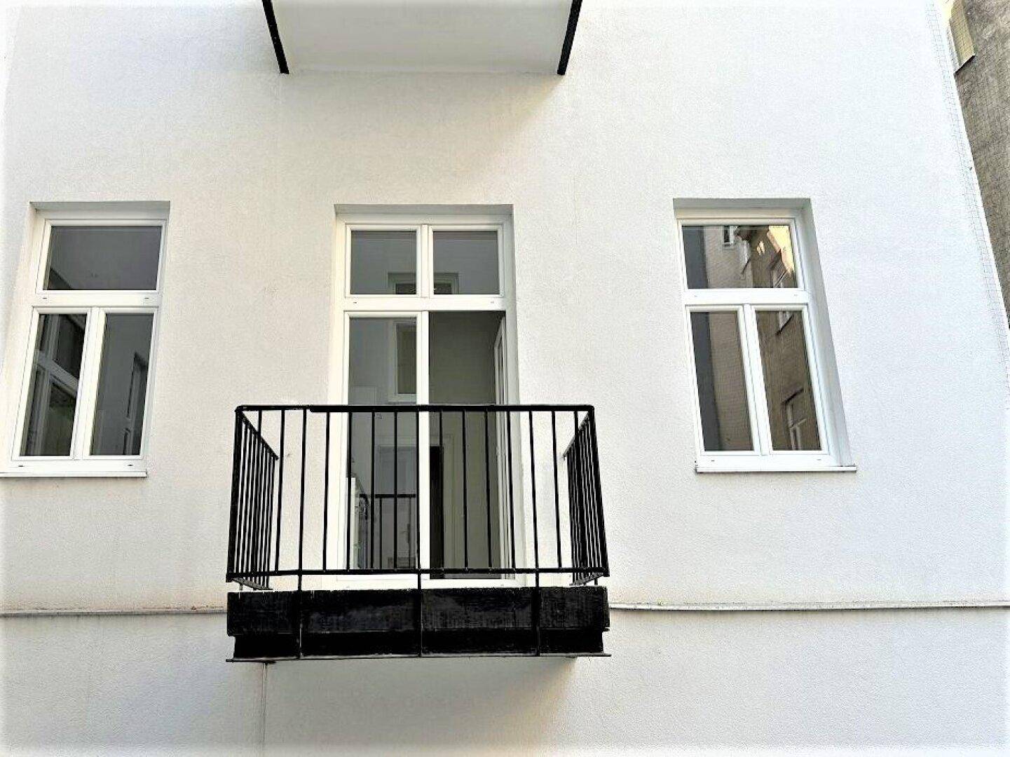 Kleiner Balkon mit schwarzem Geländer an einer weißen Fassade.