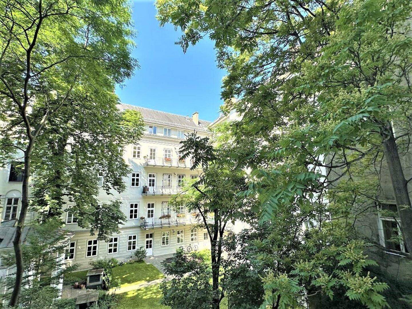 Sonnige Ansicht des grünen Innenhofs mit Bäumen und den Fassaden der umliegenden Gebäude.