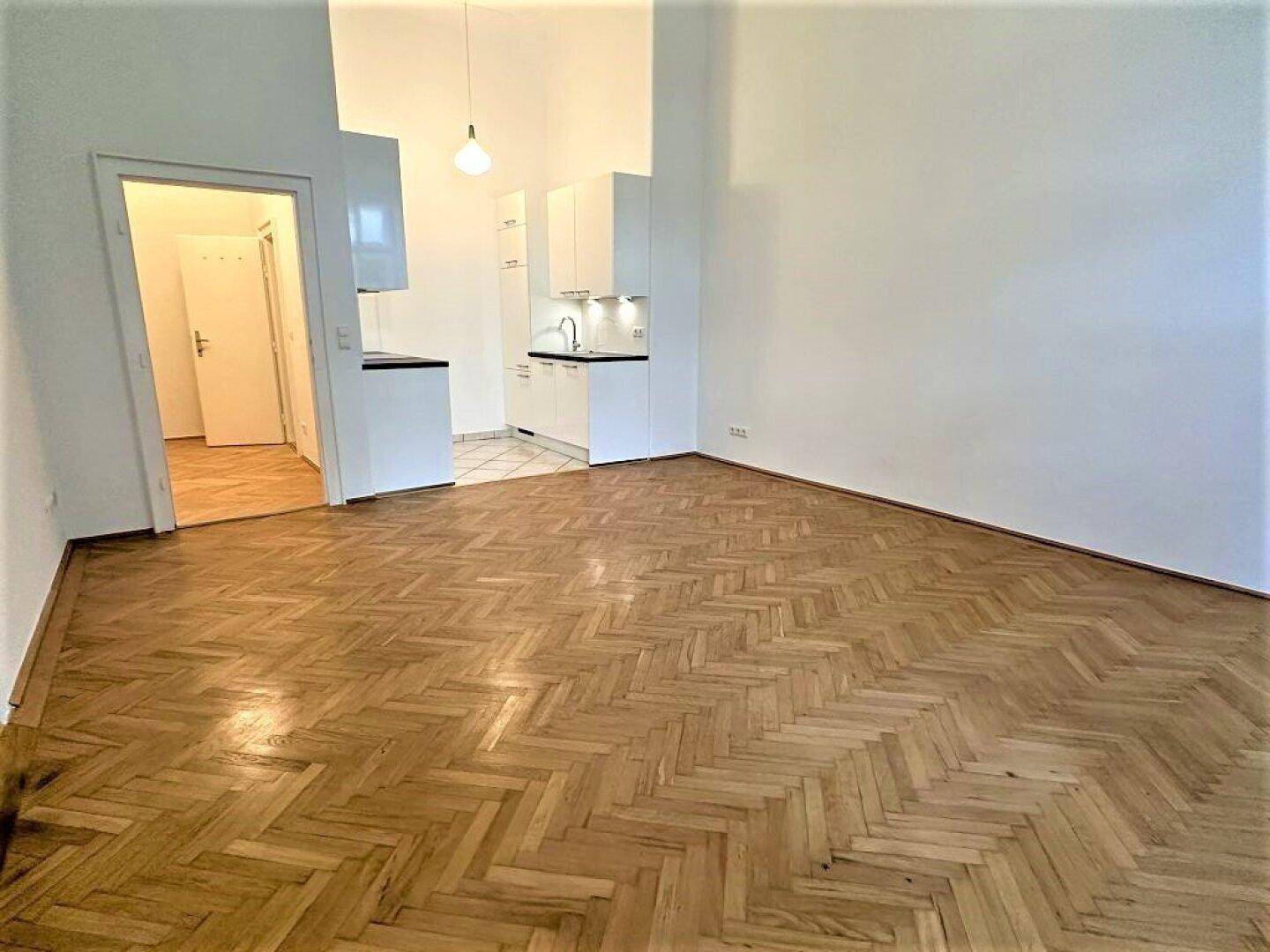 Offener Wohnbereich mit Fischgrätparkett und einer kleinen, modernen Küchenzeile.