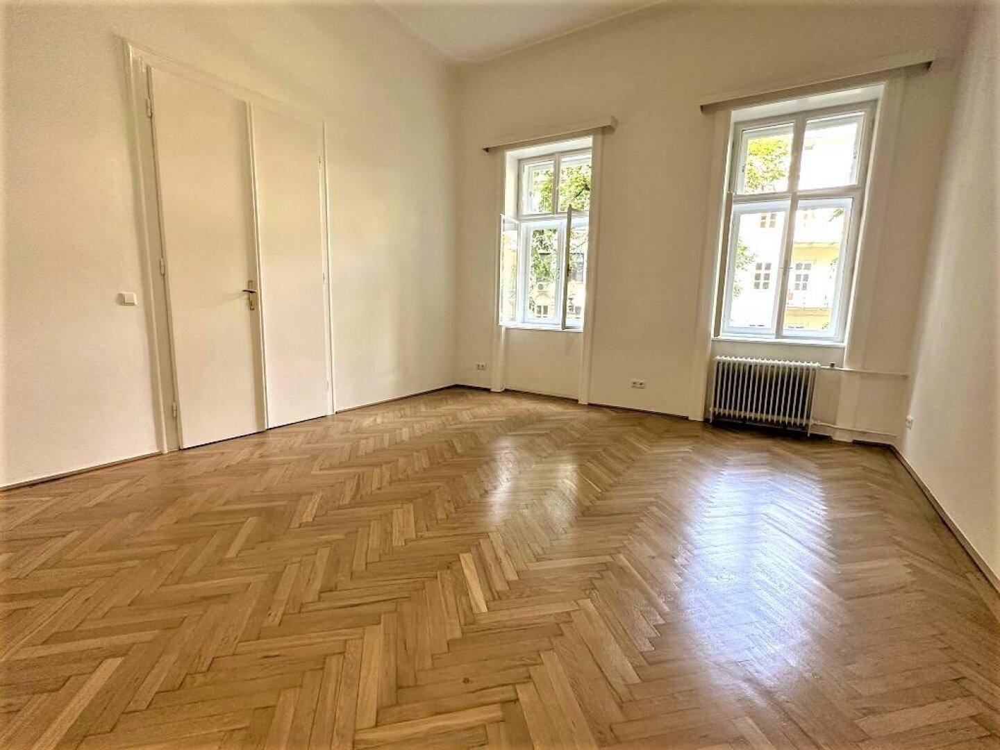 Großer, heller Raum mit Fischgrätparkett und zwei weißen Türen, ideal für flexible Nutzung.
