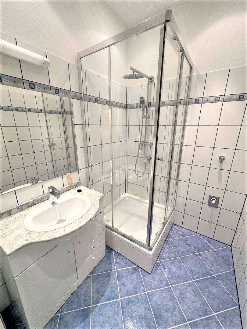 Helles Badezimmer mit Eckdusche, Waschbecken und Spiegel, gefliest in Weiß und Blau.