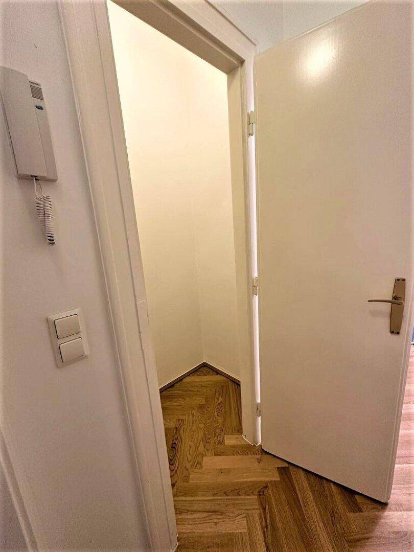 Kleiner Flur oder Abstellraum mit Parkettboden und offener Tür.
