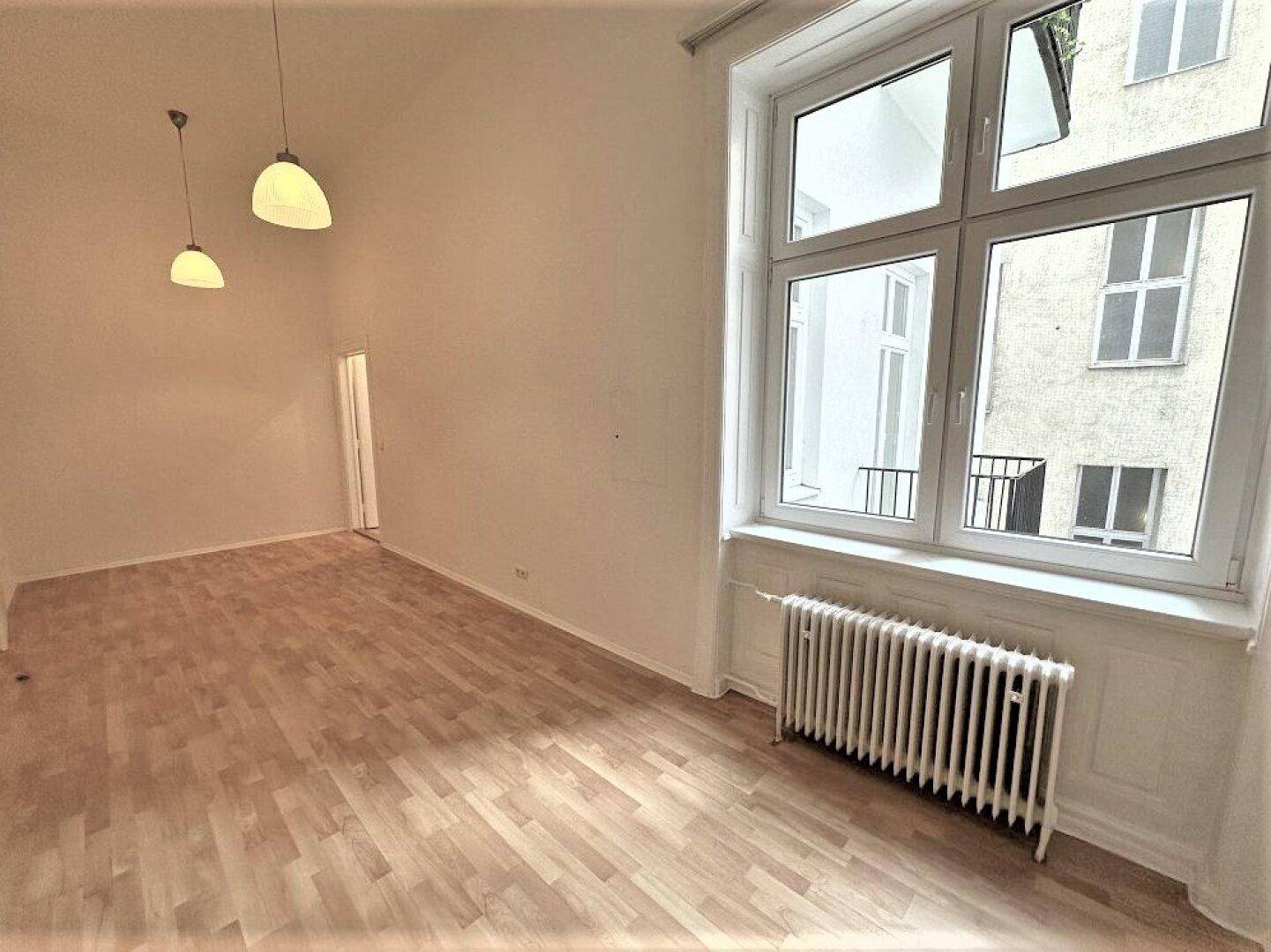 Heller Wohnraum mit hellem Parkettboden, großem Fenster und Heizkörper.