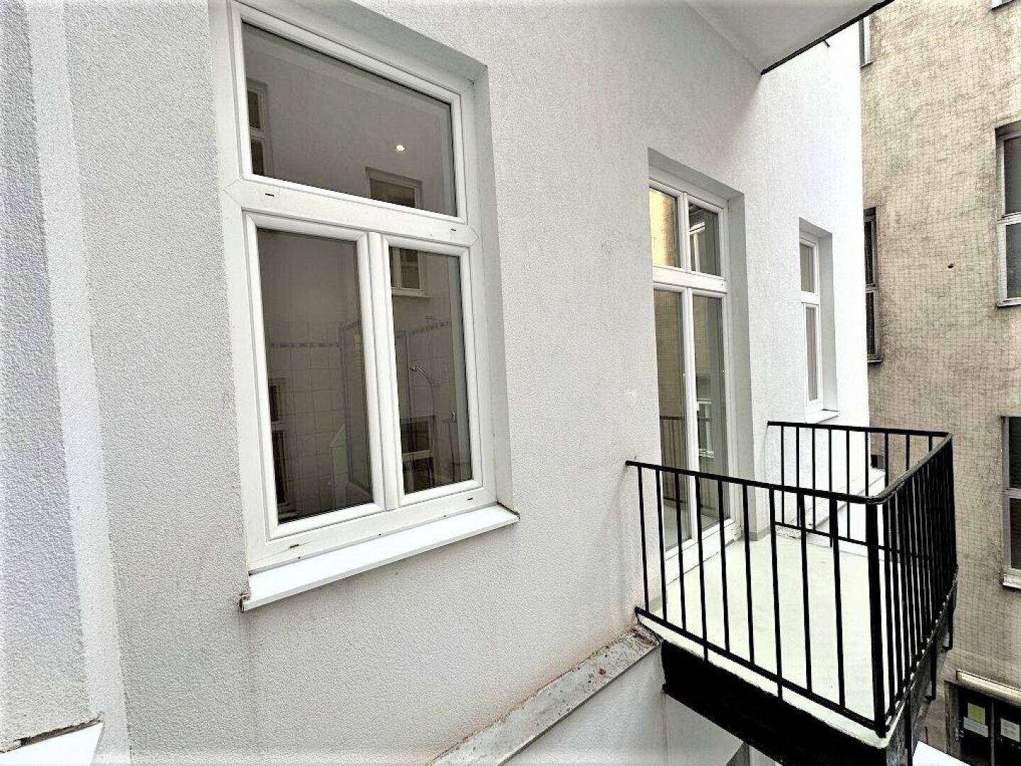 Seitlicher Blick auf einen kleinen Balkon mit schwarzem Geländer und weißer Fassade.