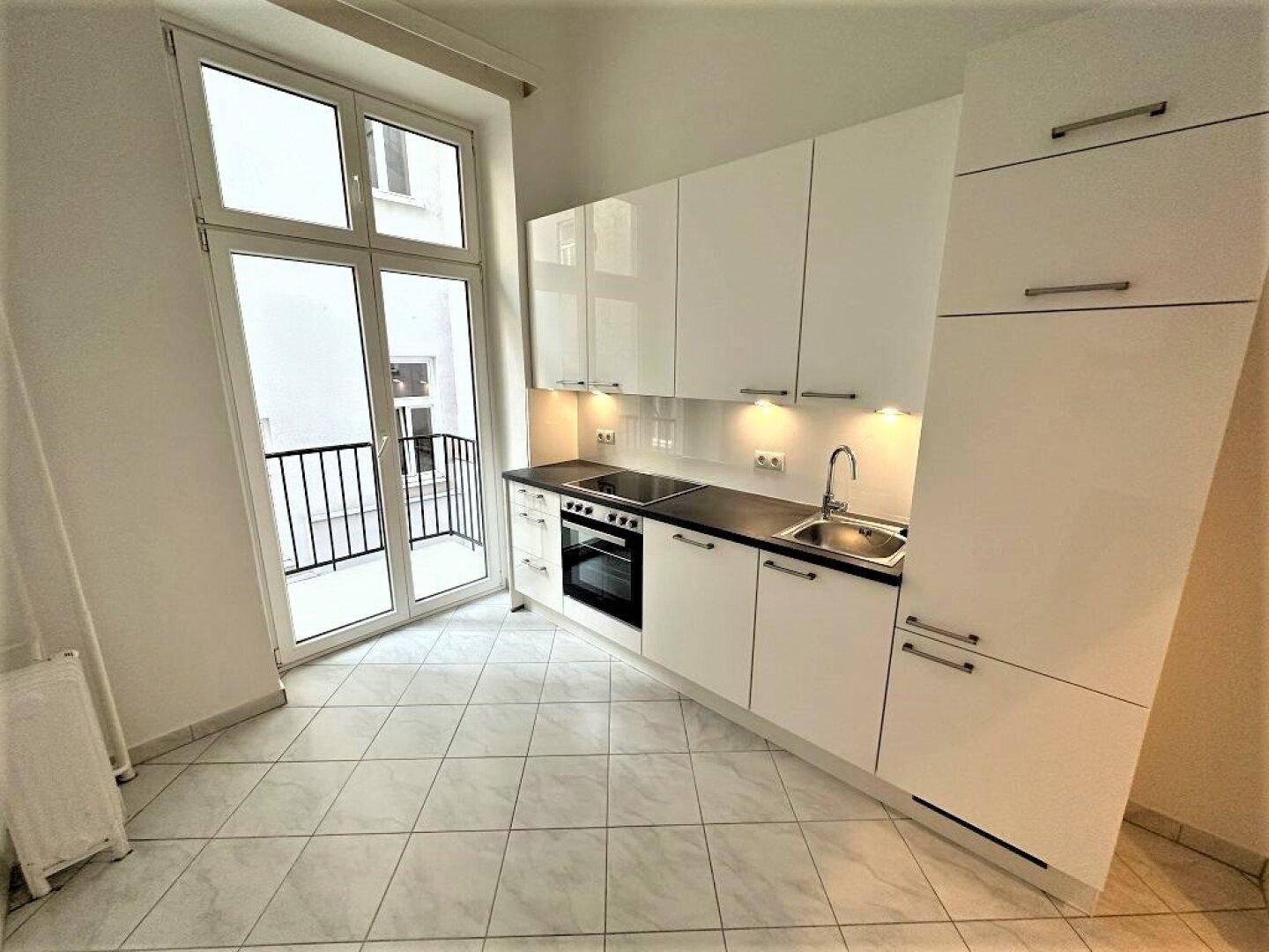 Helle Küche mit weißen Schränken, integrierten Geräten und direktem Zugang zum Balkon.