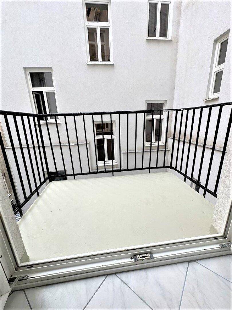 Kleiner Balkon mit weißem Boden und schwarzem Geländer, umgeben von weißen Fassaden.