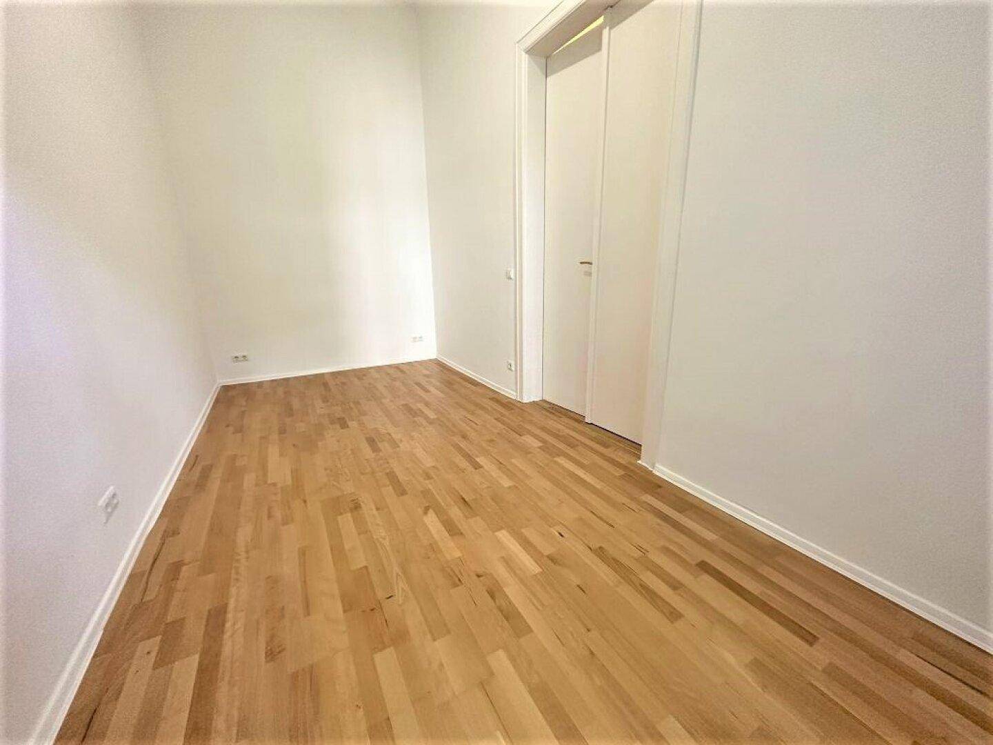Leeres Schlafzimmer mit hellem Parkettboden und zwei weißen Türen, bereit zur Einrichtung.