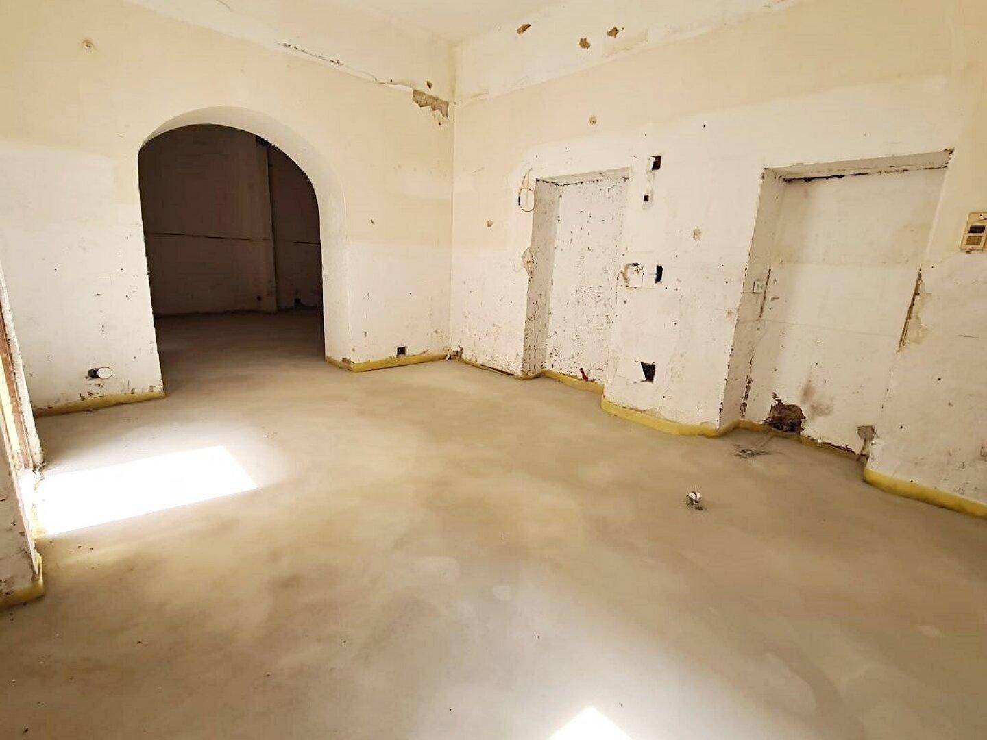 Rohbau-Innenraum mit Betonboden, freigelegten Wänden und einem Rundbogen, der zu einem weiteren Bereich führt.