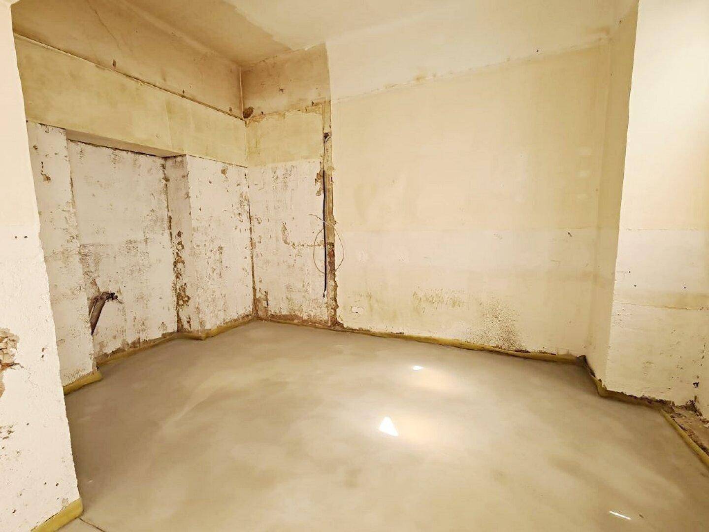 Rohbau-Innenraum mit Betonboden und teilweise freigelegten Wänden, der auf die Fertigstellung wartet.