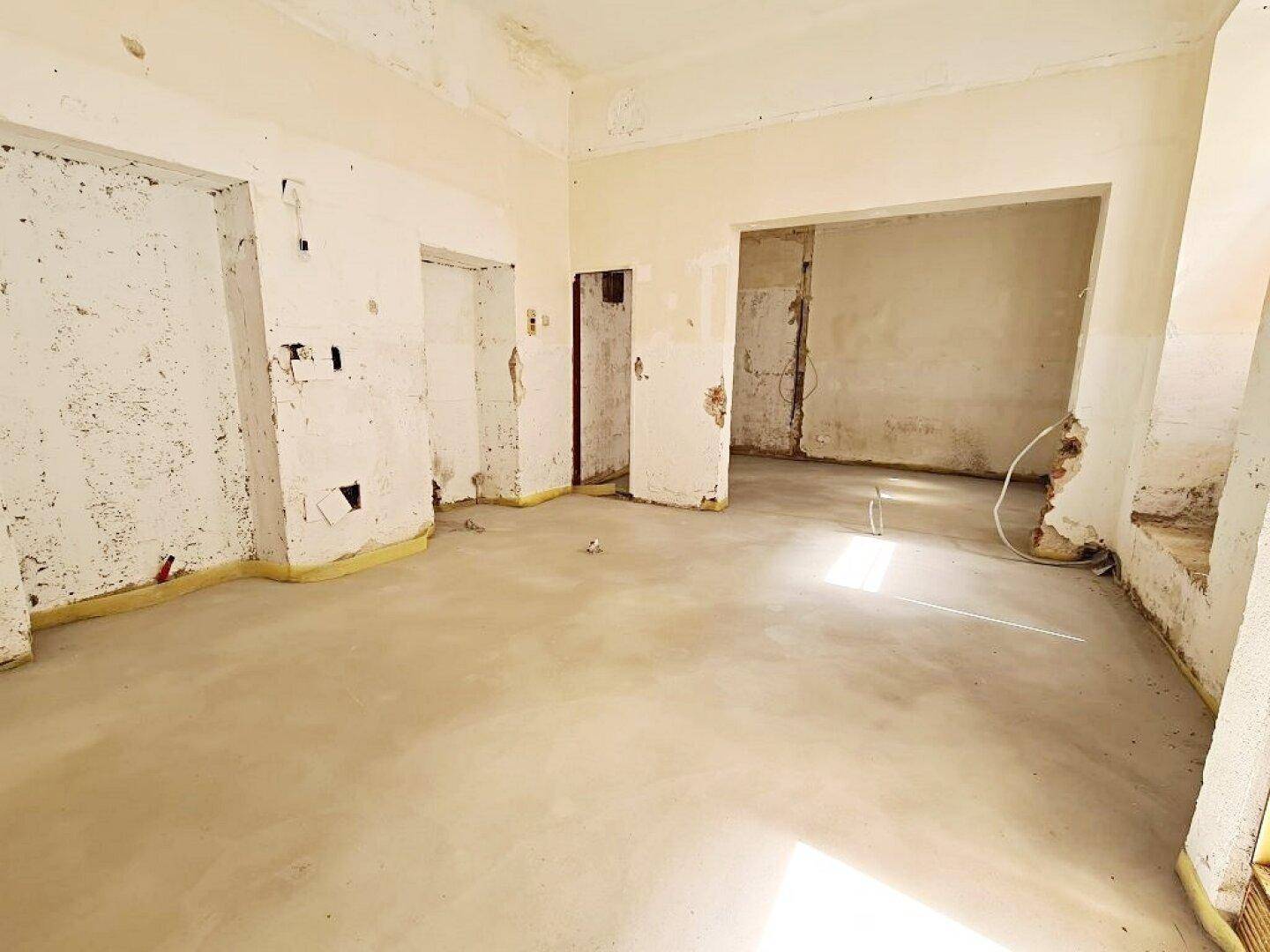 Renovierungsbedürftiger Innenraum mit Betonboden und freigelegten Wänden, der auf den Ausbau wartet.