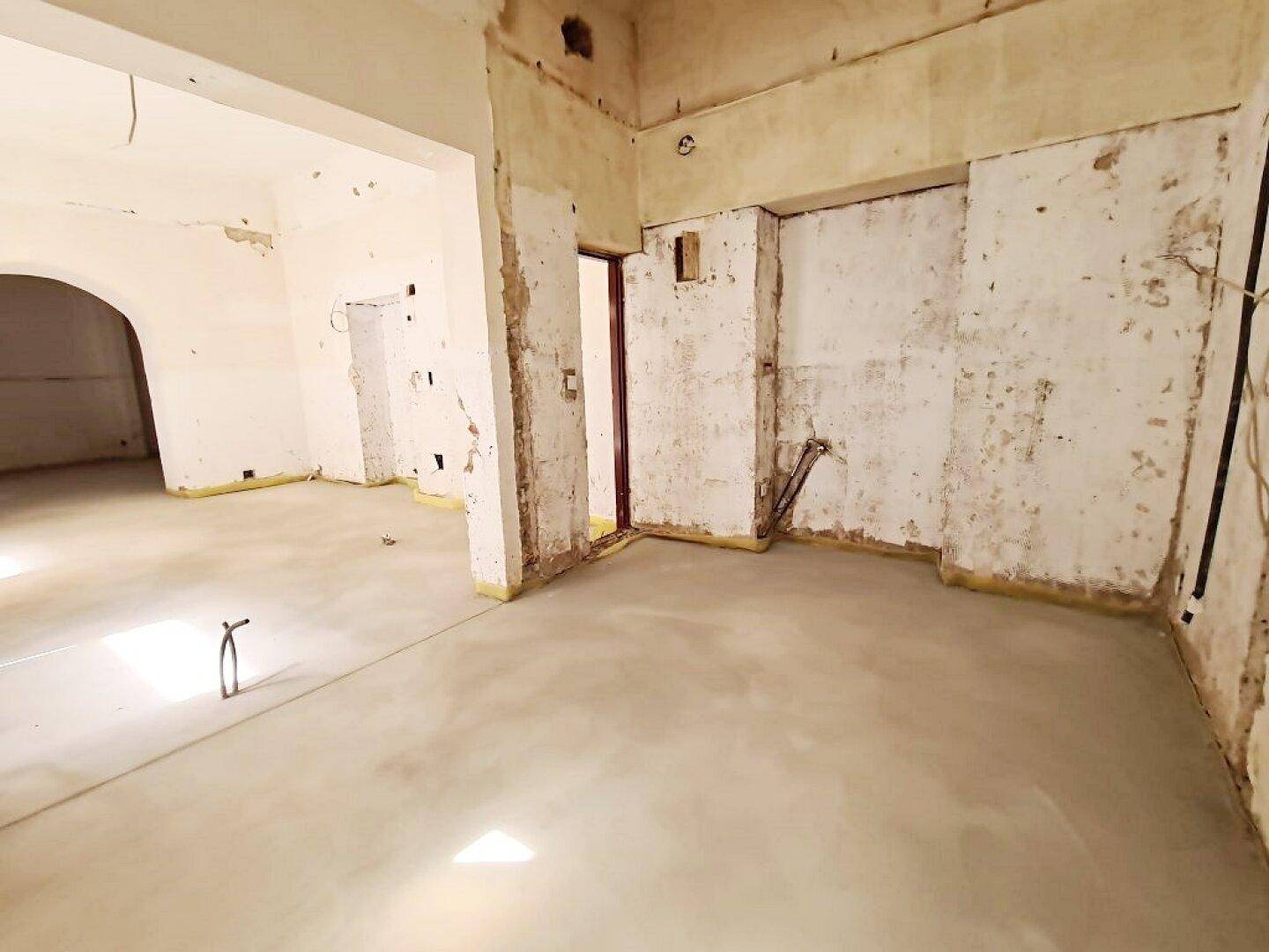 Renovierungsbedürftiger Innenraum mit Betonboden und freigelegten Wänden, der auf den Ausbau wartet.