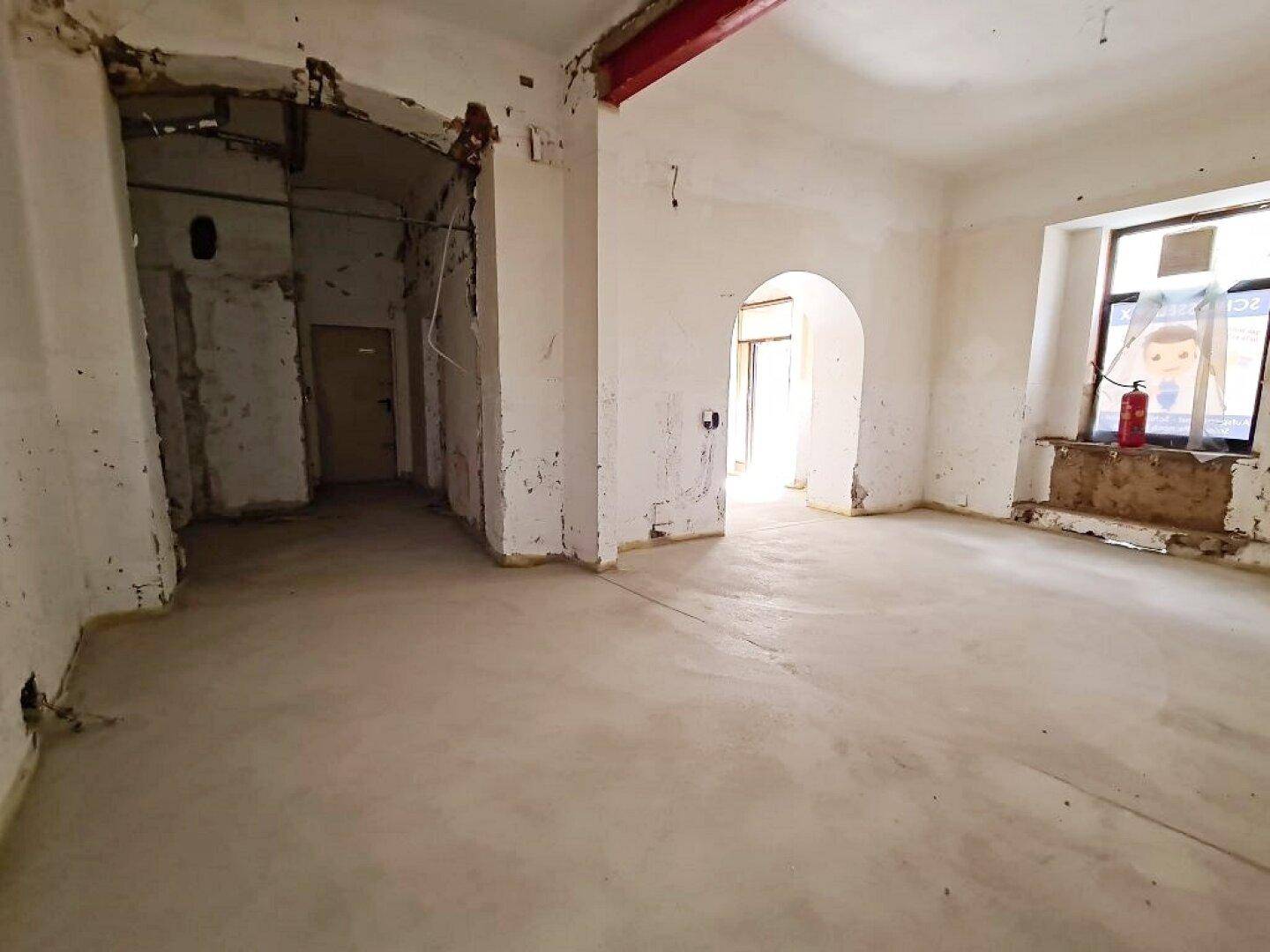 Rohbau-Innenraum mit Betonboden, freigelegten Wänden, einem Rundbogen und einem sichtbaren roten Träger.