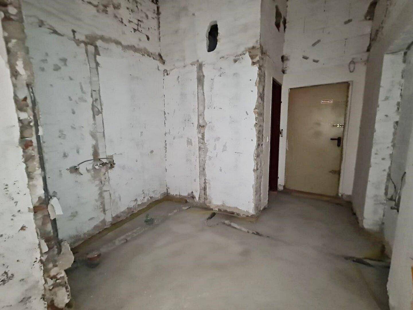 Kleiner Innenraum im Rohbauzustand mit freigelegten Wänden und einer Tür, bereit für den Ausbau.