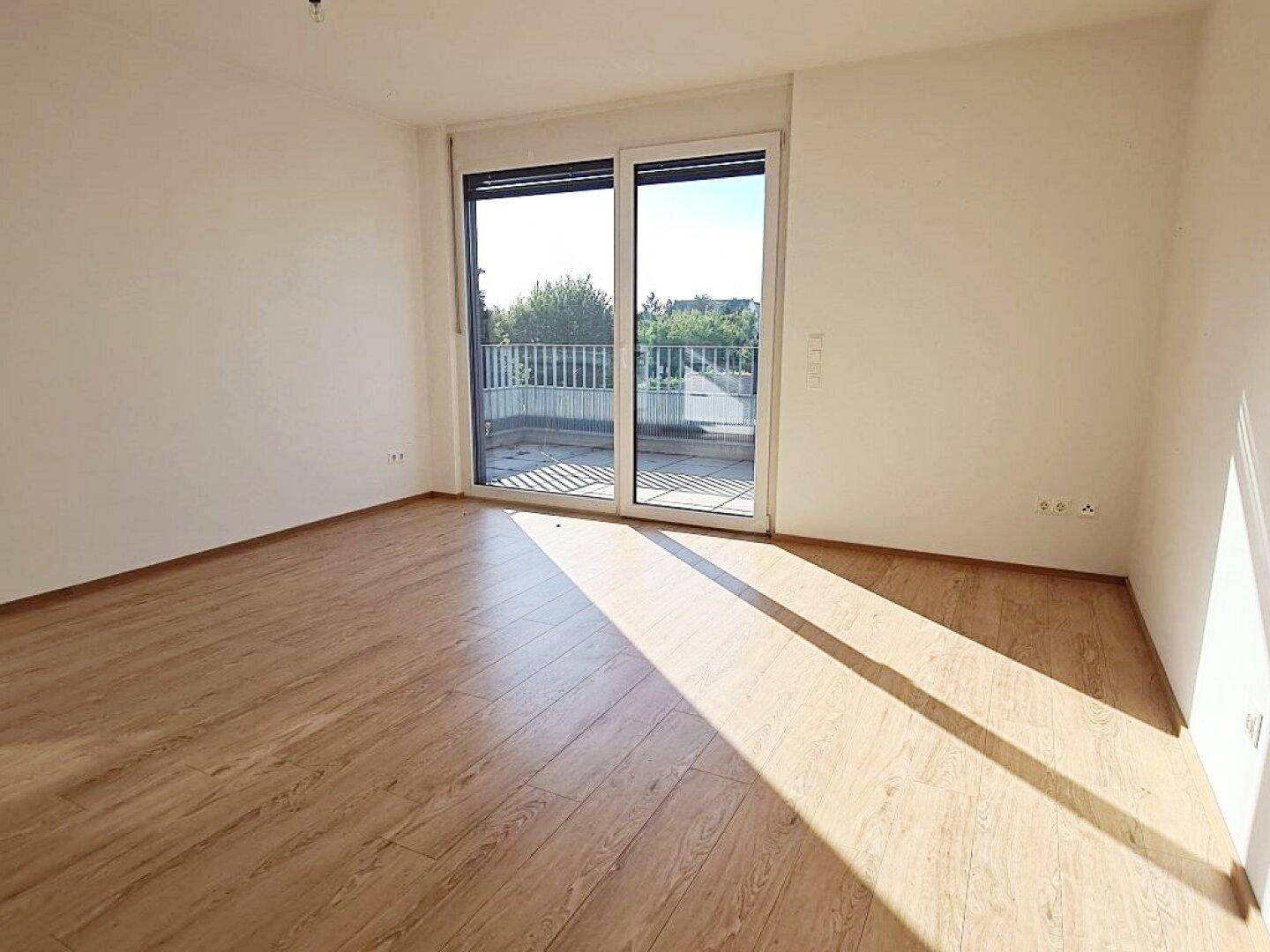 Lichtdurchfluteter Raum mit Holzboden und Zugang zu einem großen Balkon, ideal für sonnige Tage.