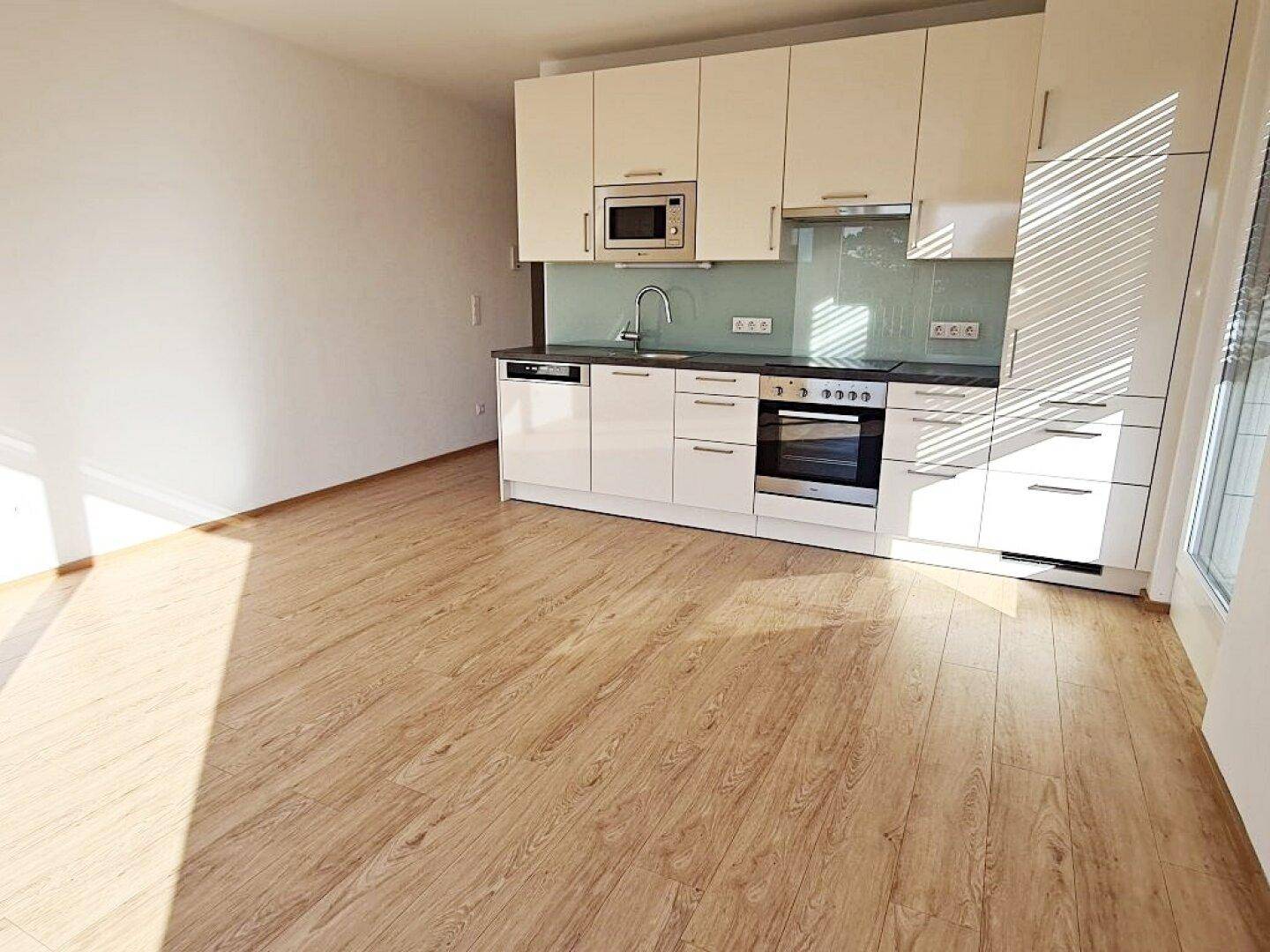 Helle Einbauküche mit modernen Geräten und Holzboden in einem offenen Wohnbereich.