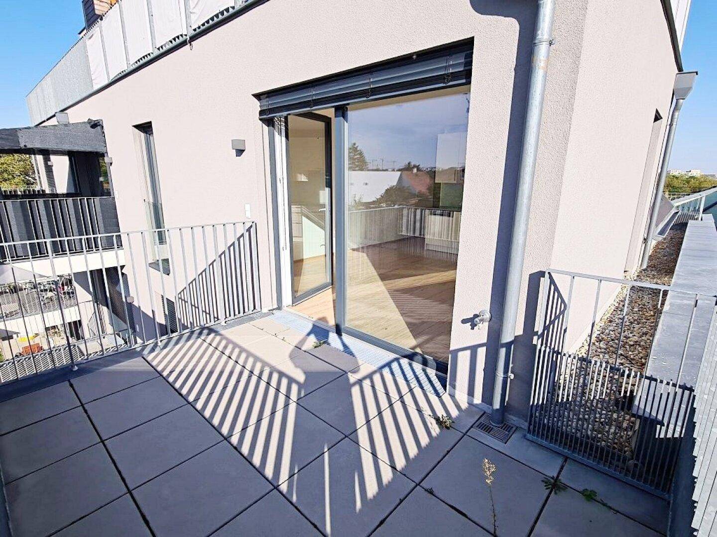 Balkon mit Fliesenboden und Schiebetür, die Zugang zu einem hellen Innenraum ermöglicht.