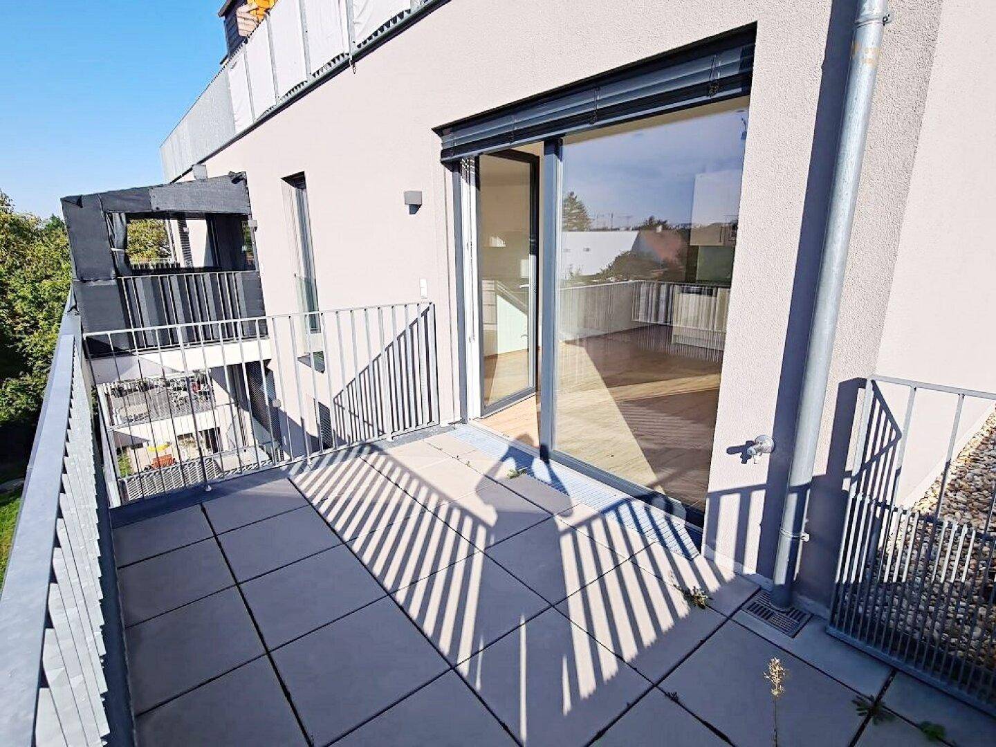 Geräumiger Balkon mit Fliesenboden und großer Glasschiebetür, die zu einem hellen Innenraum führt.