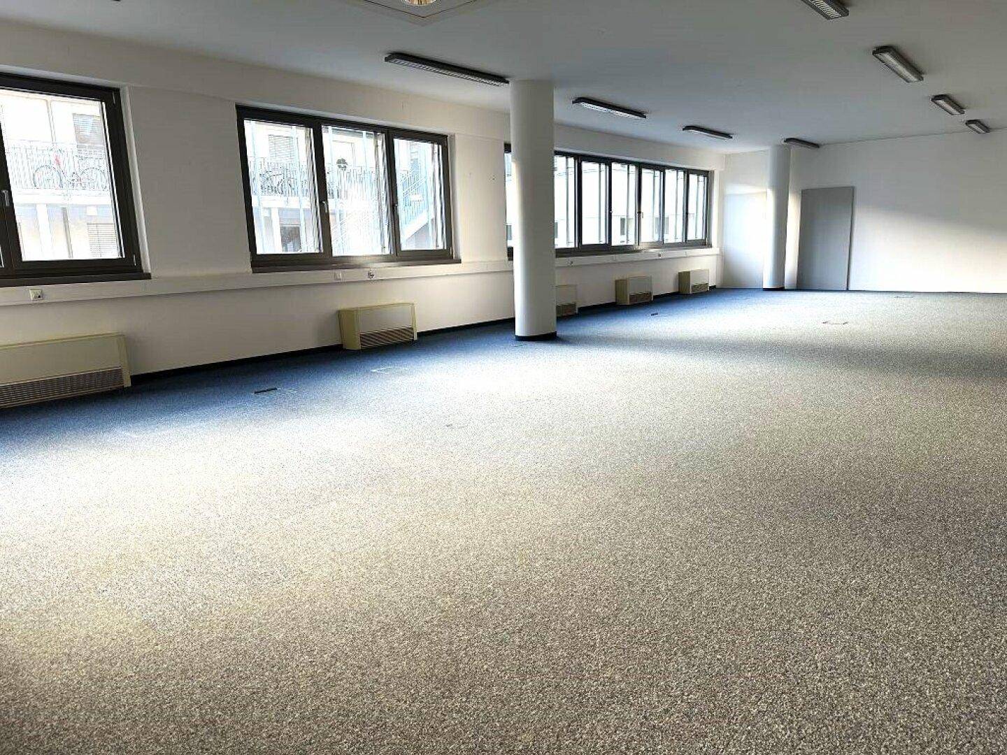 Heller Bürobereich mit Teppichboden und einer Reihe von Fenstern, die für eine angenehme Arbeitsatmosphäre sorgen.