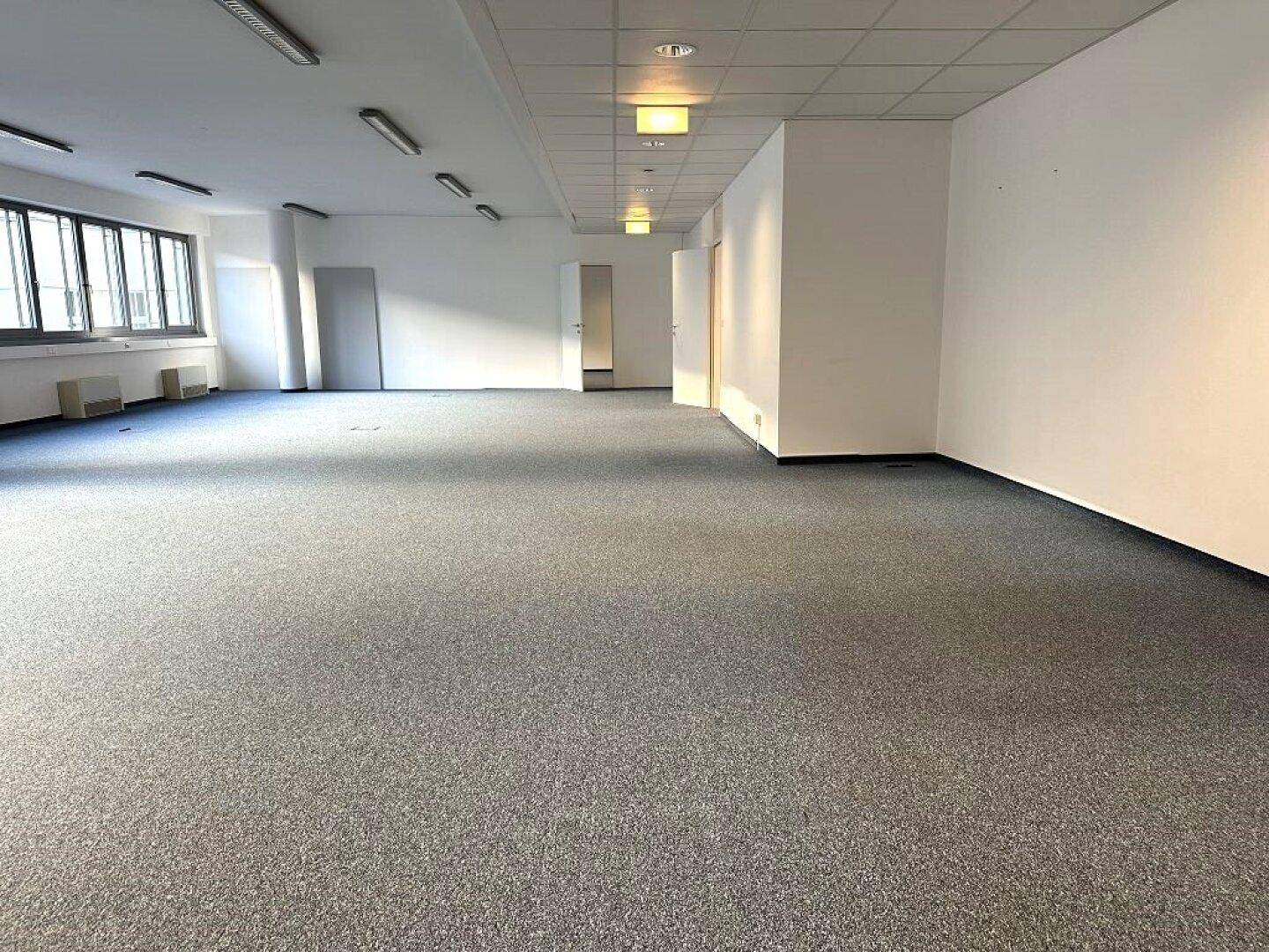 Großer, leerer Büroraum mit Teppichboden und weißen Wänden, bereit für die individuelle Gestaltung.