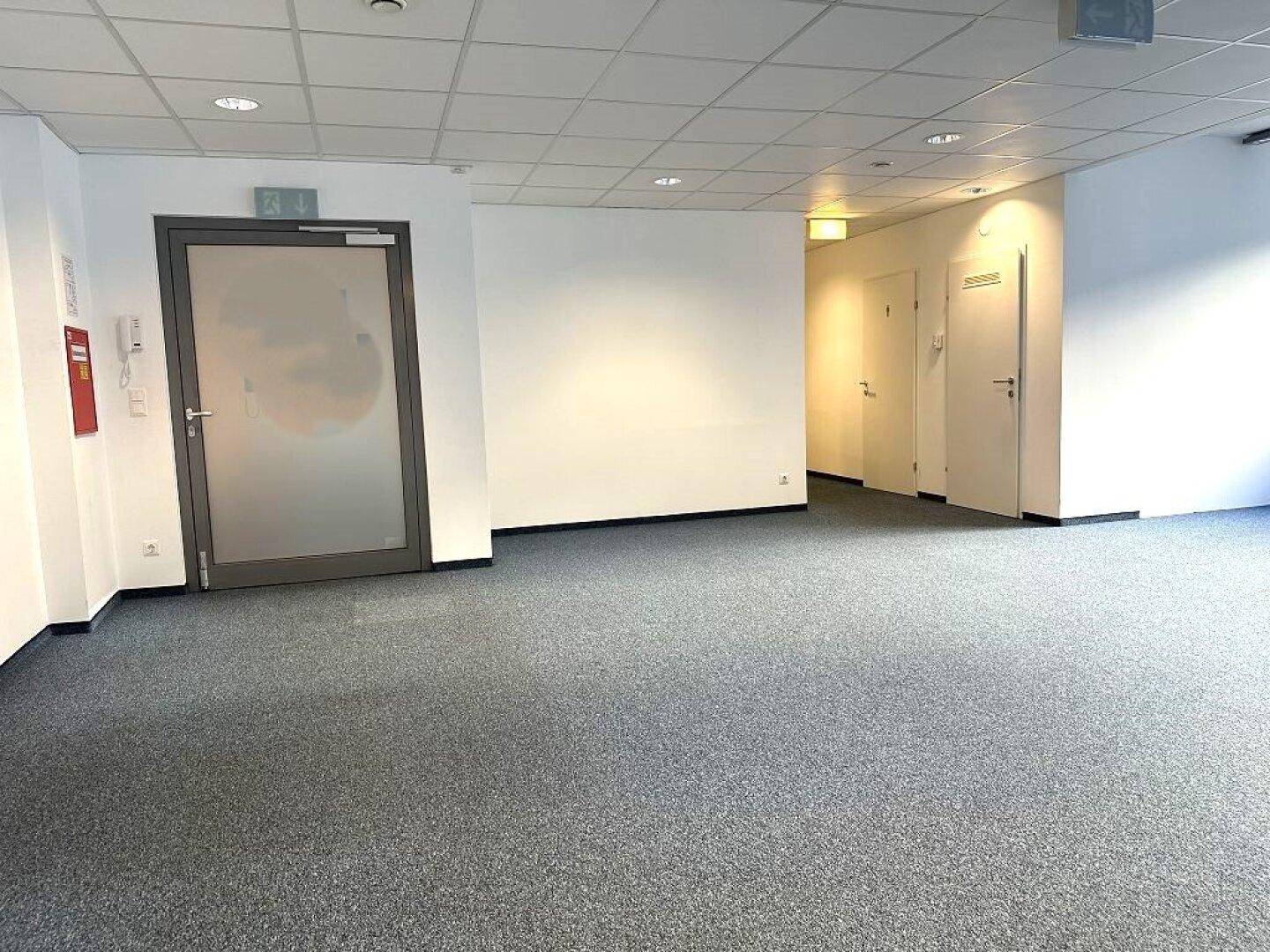 Heller Büroraum mit Teppichboden und mehreren Türen, ideal für ein flexibles Bürokonzept.