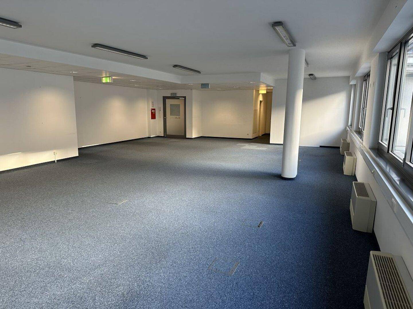Großer, heller Büroraum mit Teppichboden und mehreren Türen, bietet flexible Gestaltungsmöglichkeiten.