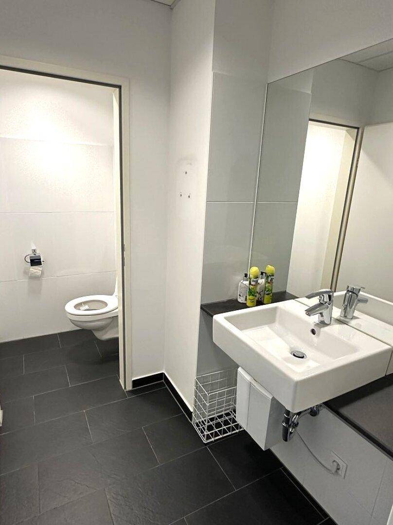 Modernes Badezimmer mit dunklen Fliesen, weißem Waschbecken und wandmontierter Toilette.