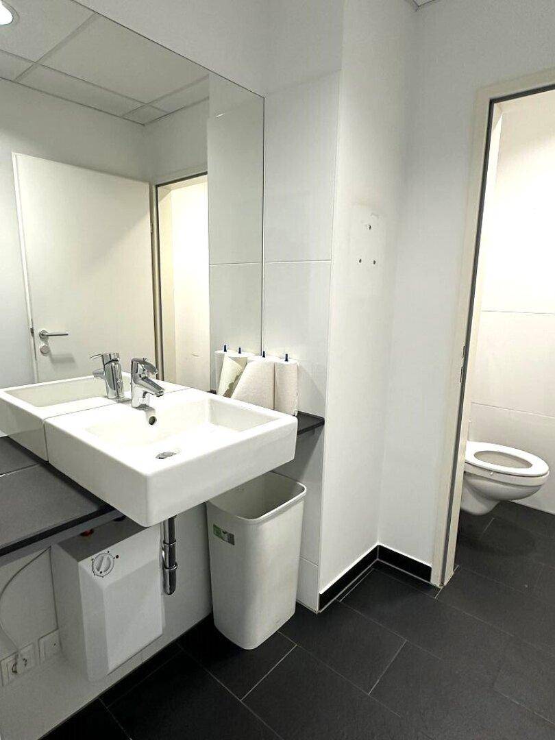 Helles Badezimmer mit großem Spiegel, modernem Waschbecken und dunklem Fliesenboden.