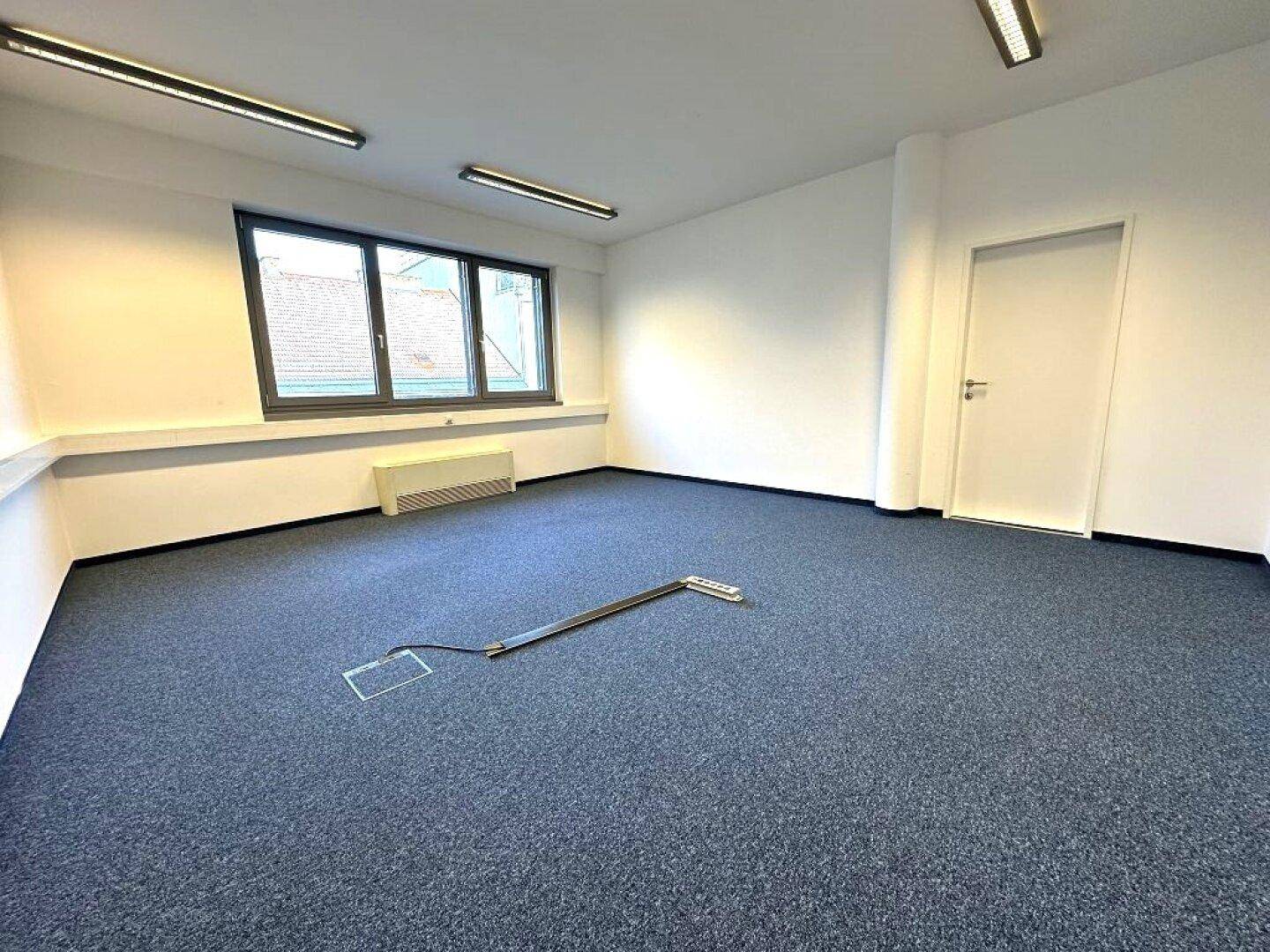 Geräumiger Büroraum mit Teppichboden und weißen Wänden, bietet viel Platz für individuelle Gestaltung.