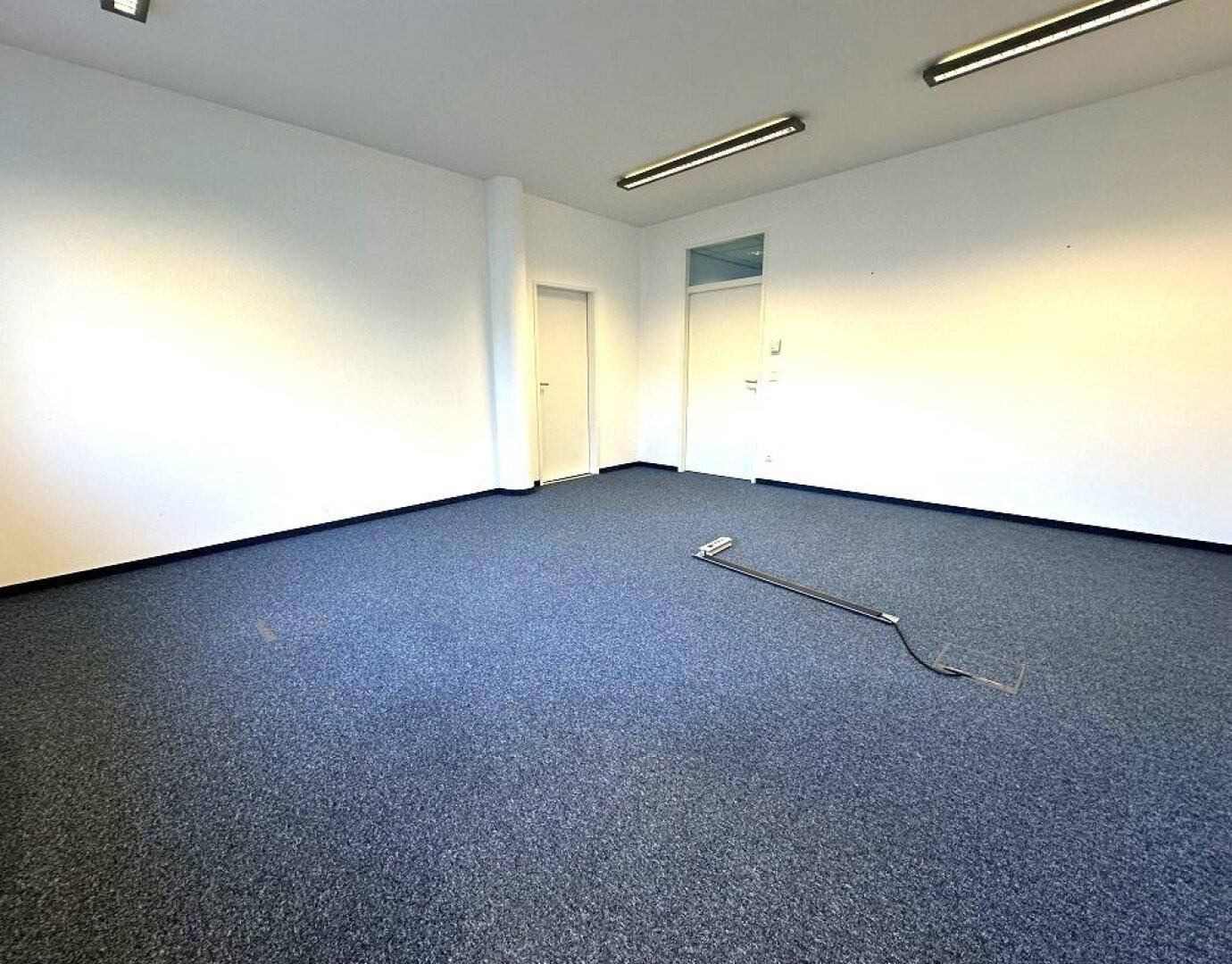 Heller Büroraum mit Teppichboden und weißen Wänden, ideal für ein produktives Arbeitsumfeld.