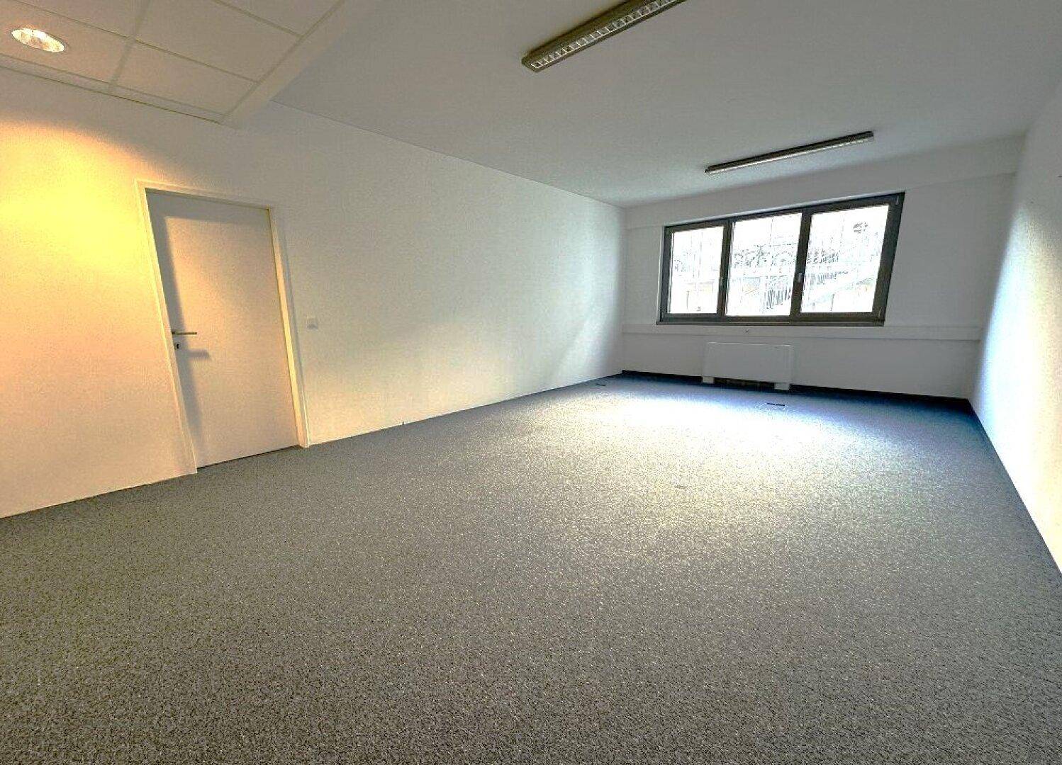 Geräumiger Büroraum mit Teppichboden und weißen Wänden, bietet viel Platz für individuelle Gestaltung.