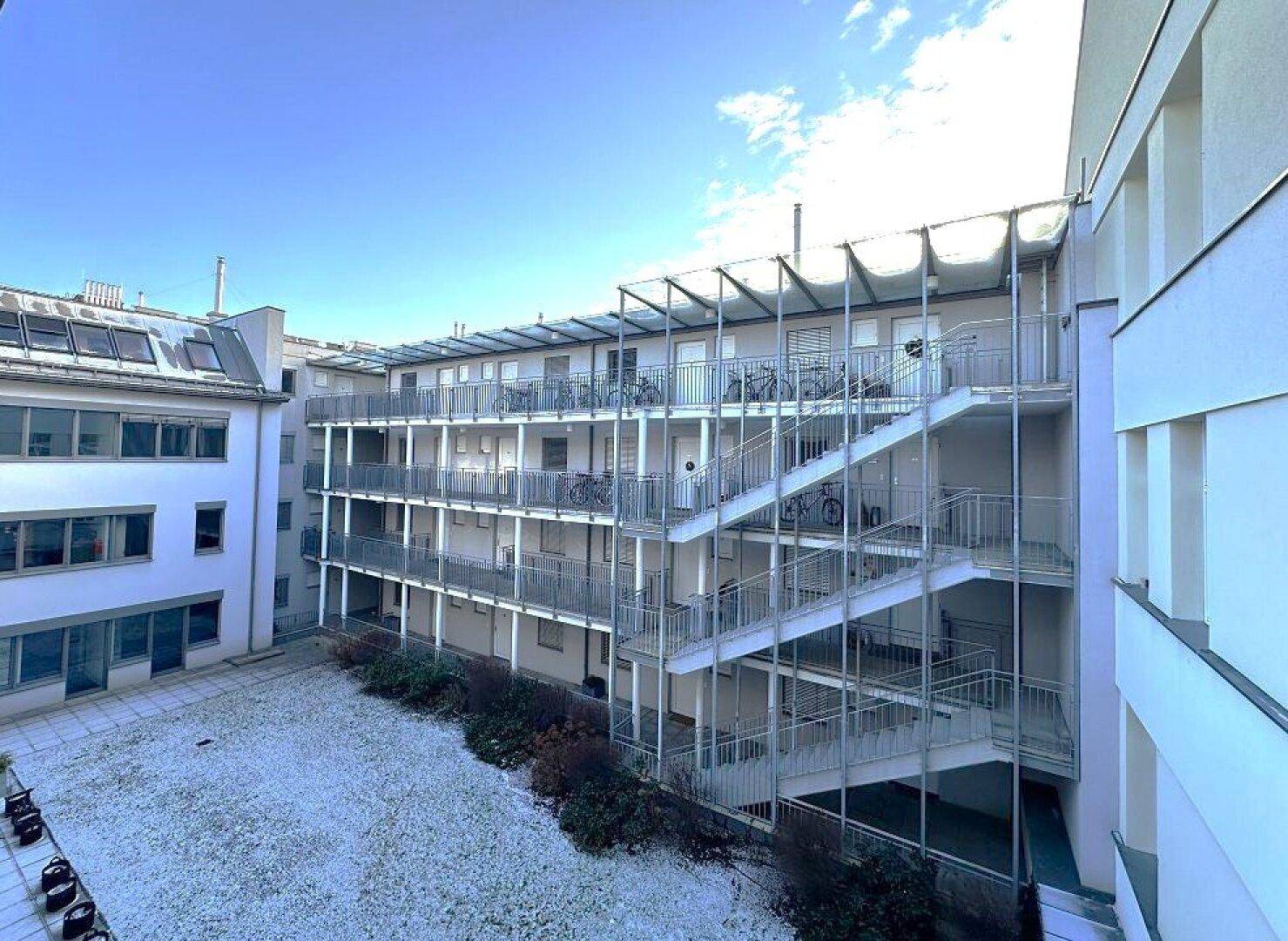 Innenhof eines Gebäudekomplexes mit Außentreppen und Fahrradständern, teilweise schneebedeckt.