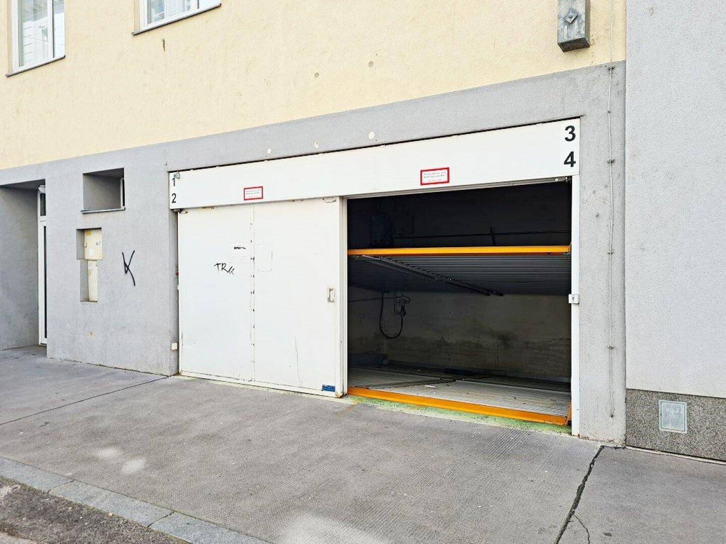 Teilweise geöffnete Tiefgarageneinfahrt an der Gebäudefassade mit Blick auf das mechanische Parksystem.