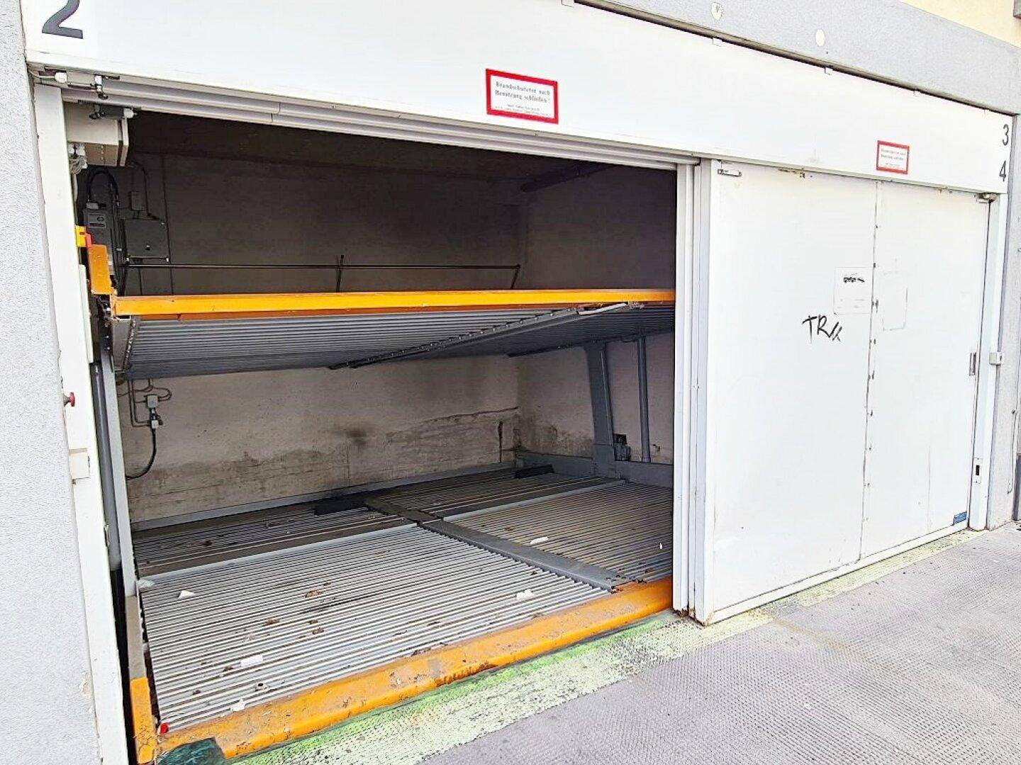 Eingang zur Tiefgarage mit geöffnetem Tor und sichtbarem mechanischem Parksystem im Inneren.