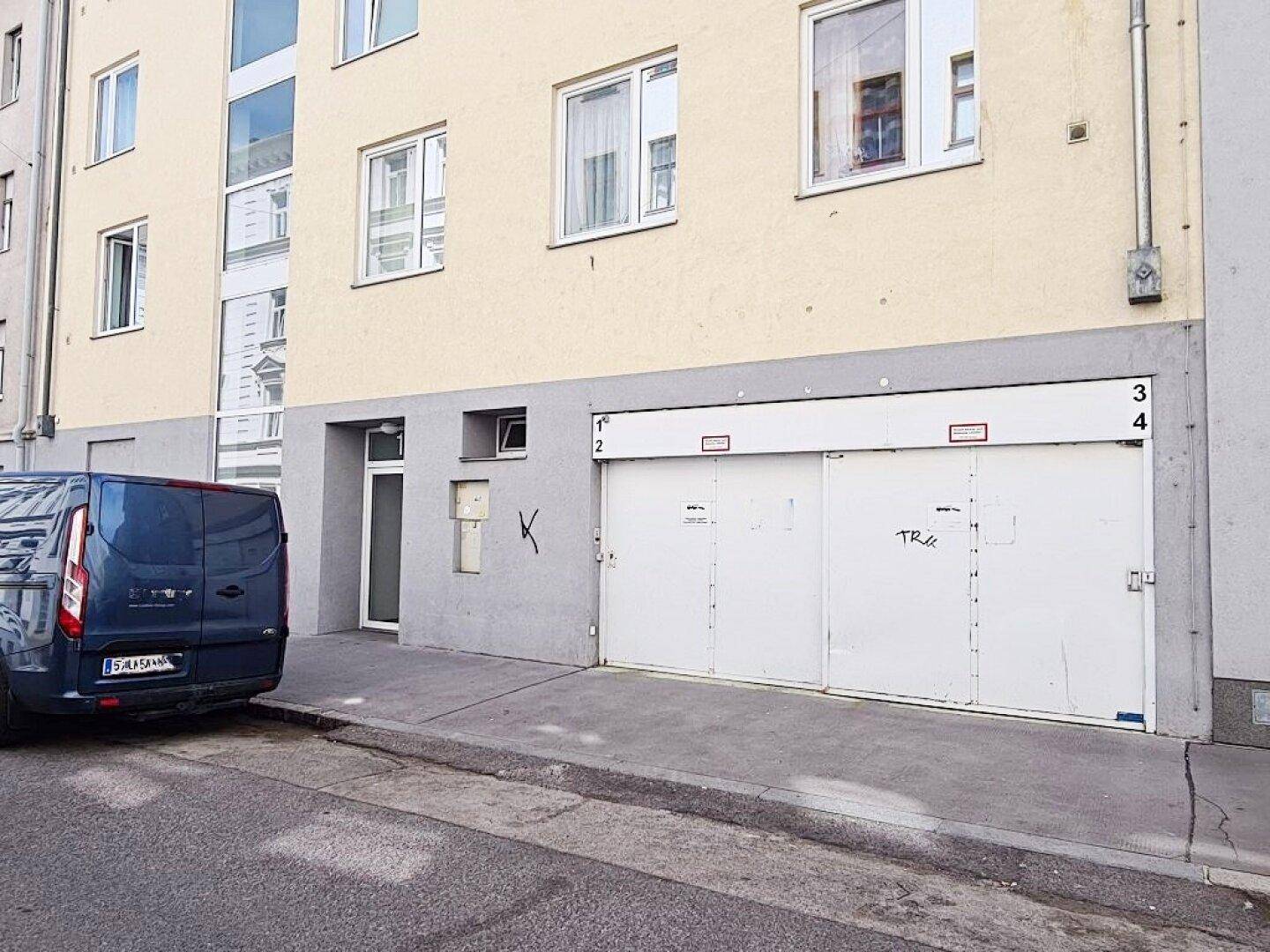 Gebäudefassade mit geschlossener Tiefgarageneinfahrt und einem geparkten Lieferwagen davor auf der Straße.