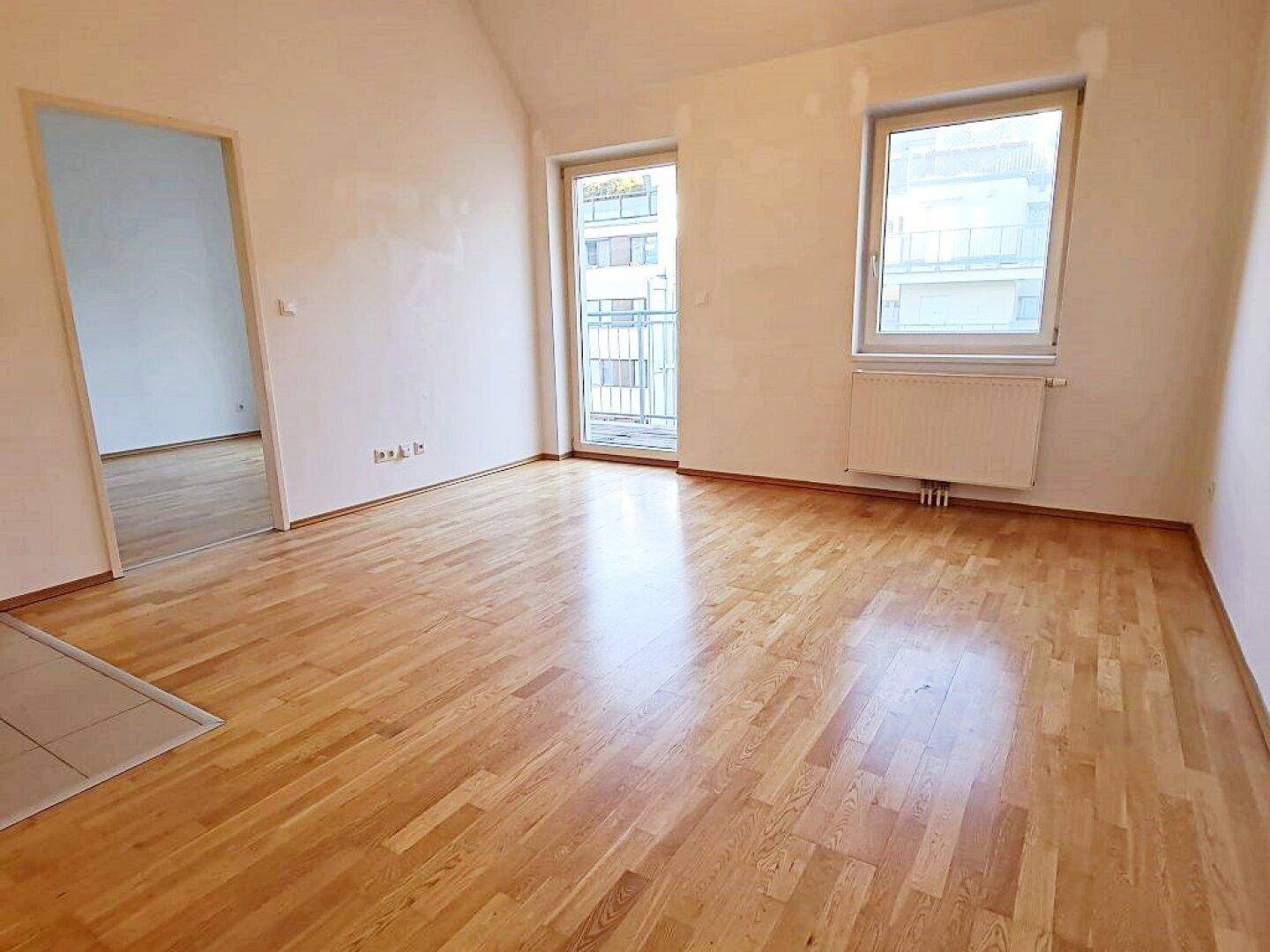 Helles Zimmer mit Parkettboden und Zugang zu einem Balkon, ideal als Wohn- oder Schlafbereich.