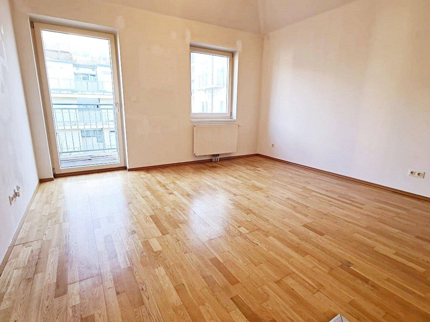 Helles Zimmer mit Parkettboden und Balkonzugang, bereit zur individuellen Gestaltung.