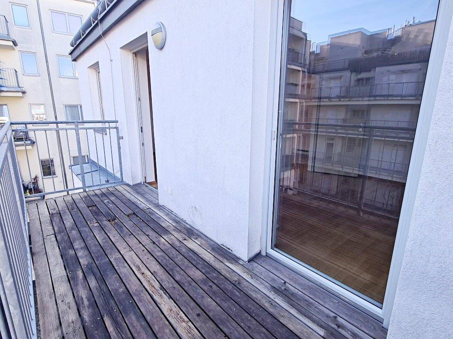 Balkon mit Holzdielen und Metallgeländer, bietet einen Blick auf die umliegenden Gebäude.