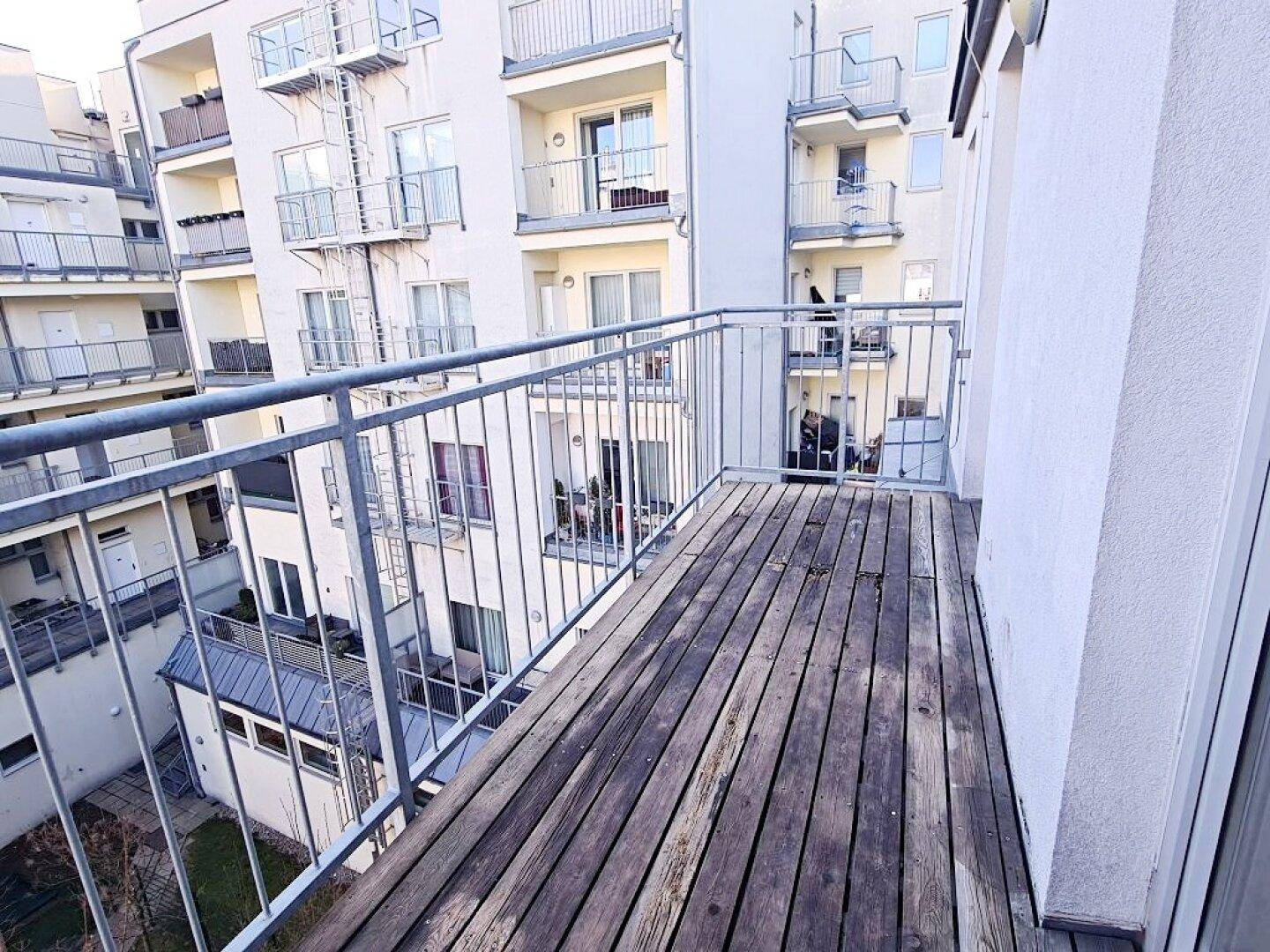 Geräumiger Balkon mit Holzdielen und Blick auf den Innenhof des Wohnkomplexes.