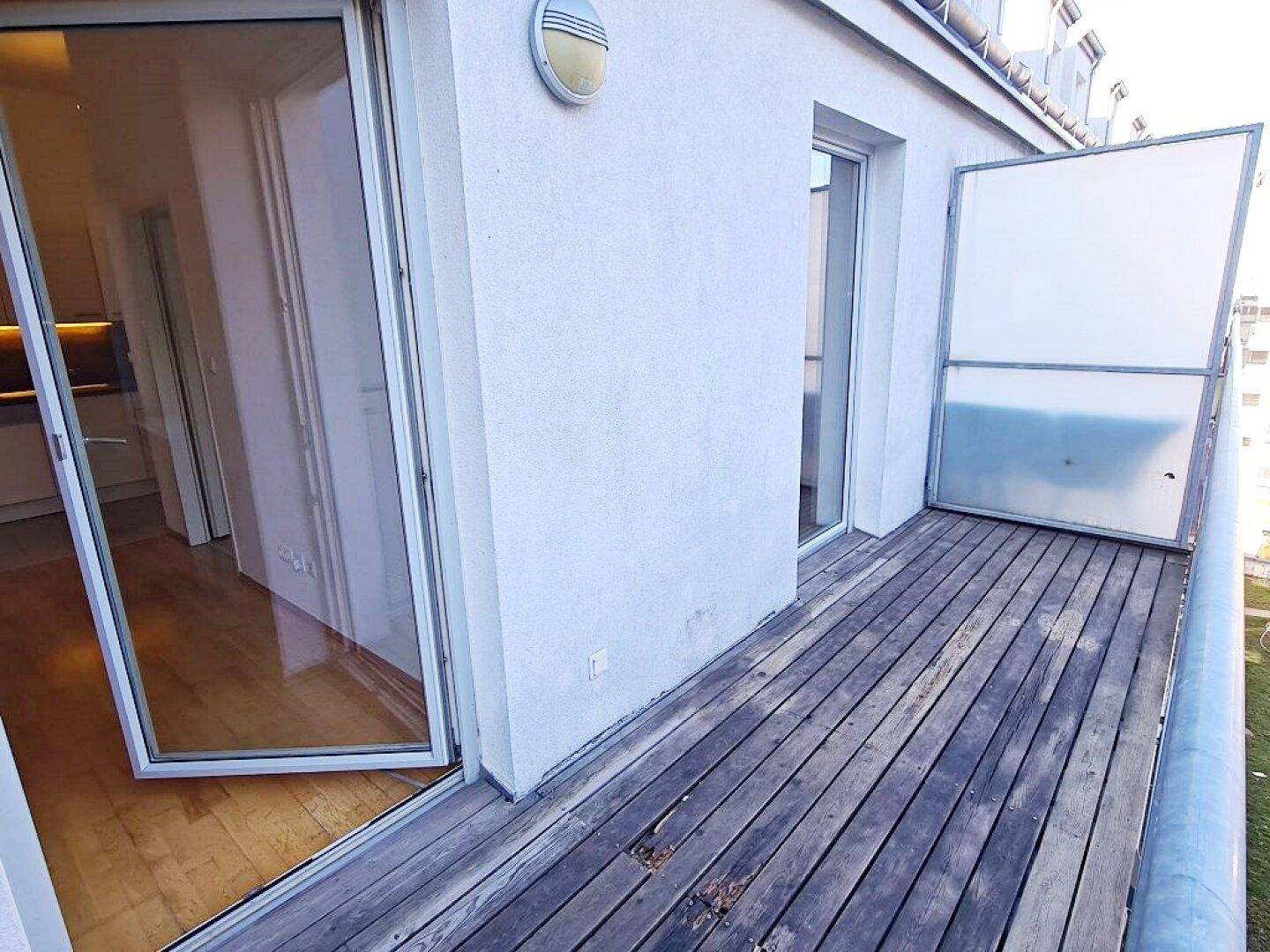 Balkon mit Holzdielen und Zugang zum Innenraum, ideal für frische Luft.
