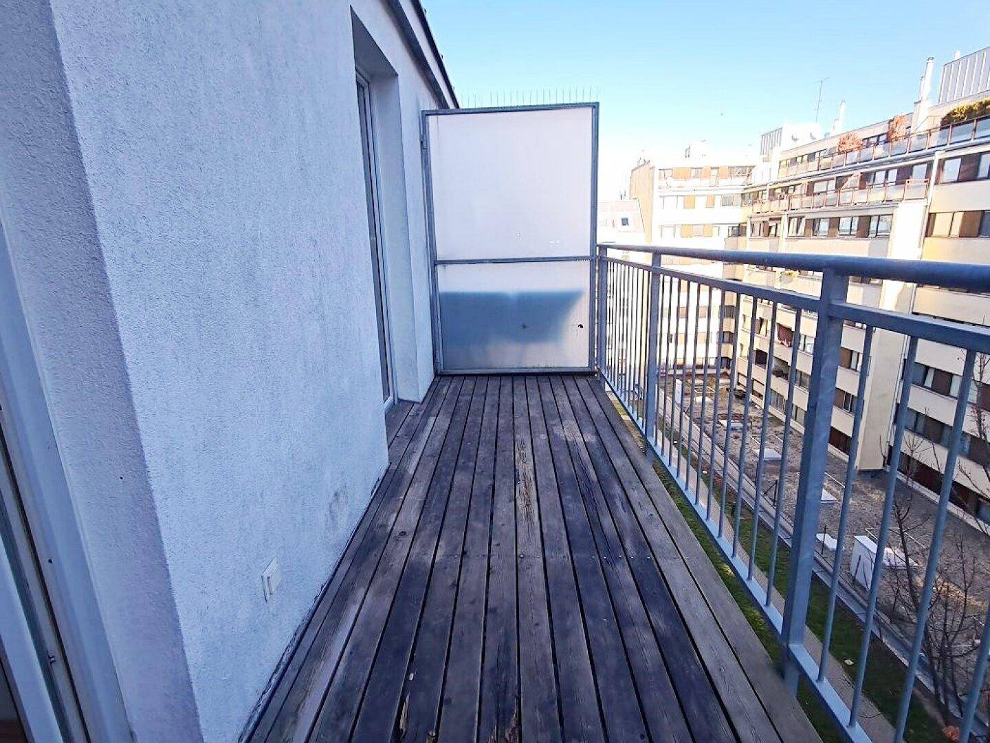 Langer Balkon mit Holzdielen und Metallgeländer, bietet eine weite Aussicht über die Stadt.