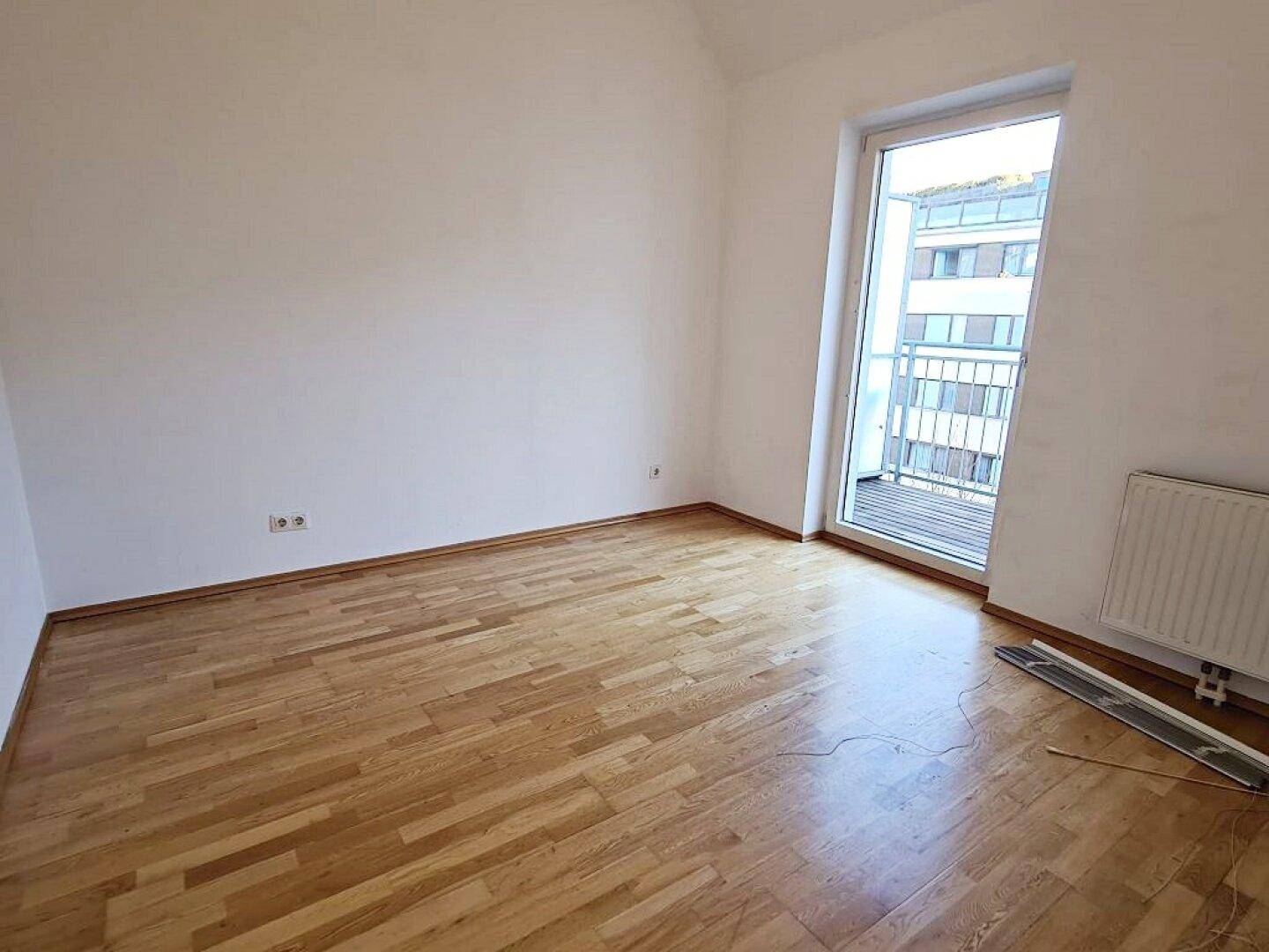 Geräumiges Zimmer mit Parkettboden und Balkonzugang, ideal für Schlaf- oder Arbeitszimmer.