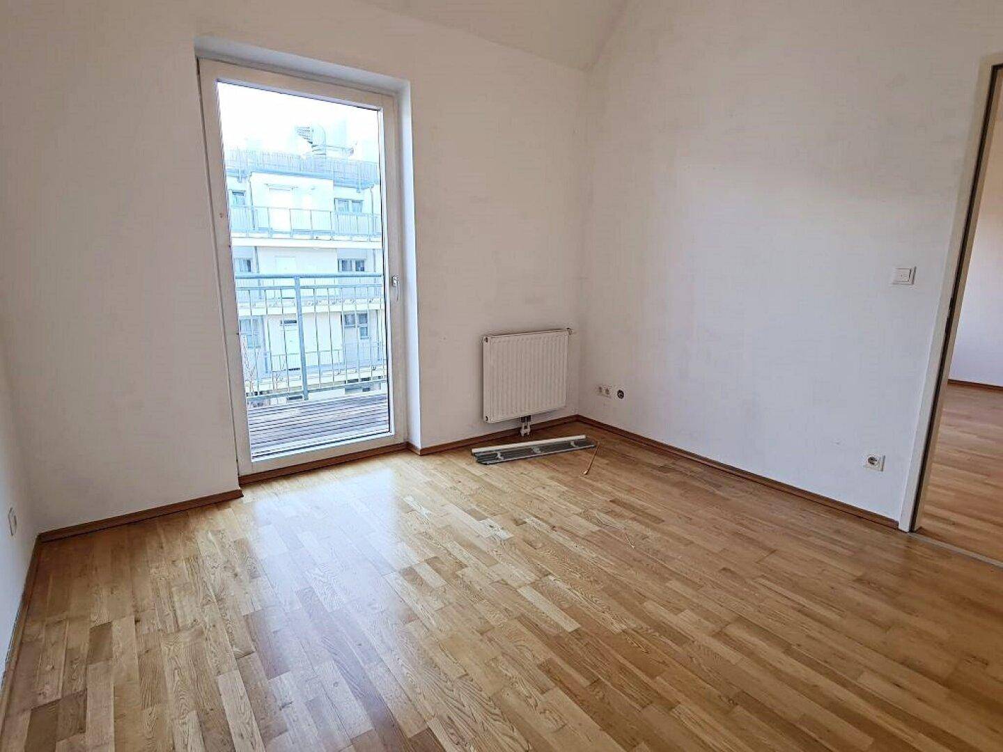 Lichtdurchflutetes Zimmer mit Parkettboden und Balkonzugang, bereit zur individuellen Einrichtung.