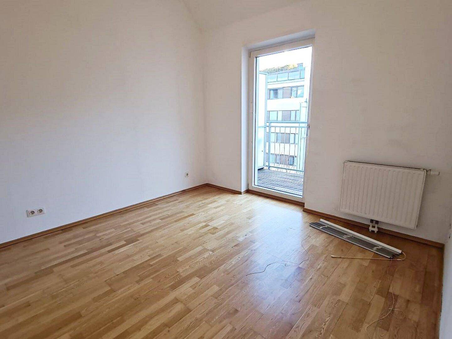 Helles Zimmer mit Parkettboden und Balkonzugang, bietet eine ruhige Atmosphäre.