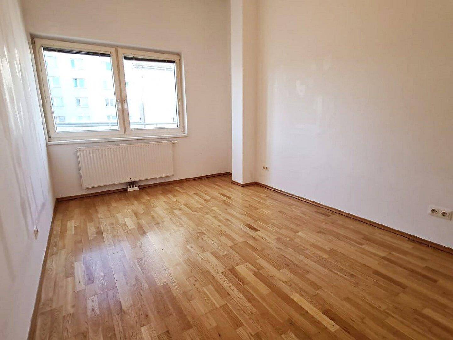 Geräumiges Zimmer mit Parkettboden und großem Fenster, sorgt für viel Tageslicht.