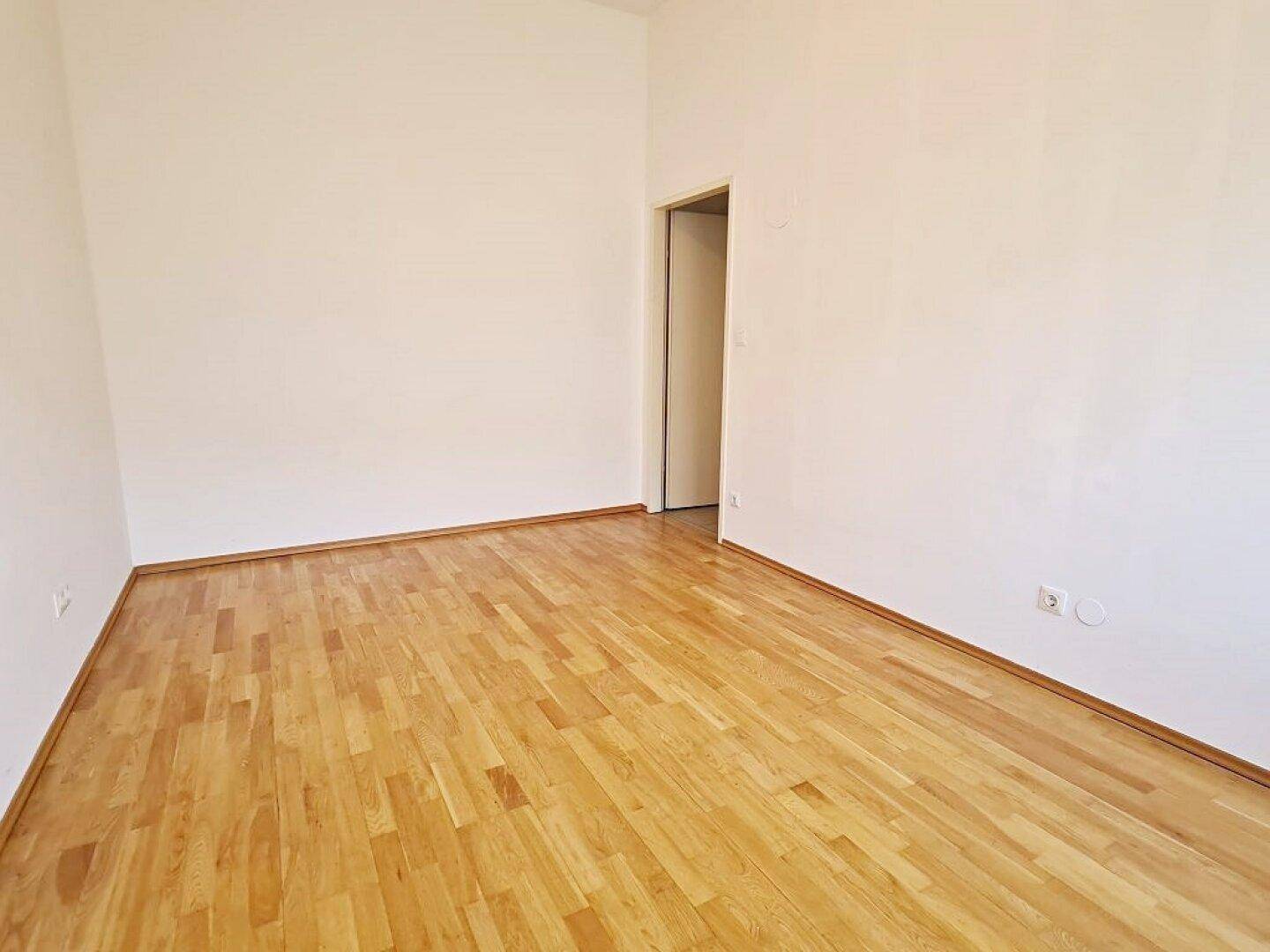 Ruhiges Zimmer mit Parkettboden und weiß gestrichenen Wänden, bietet eine neutrale Basis.