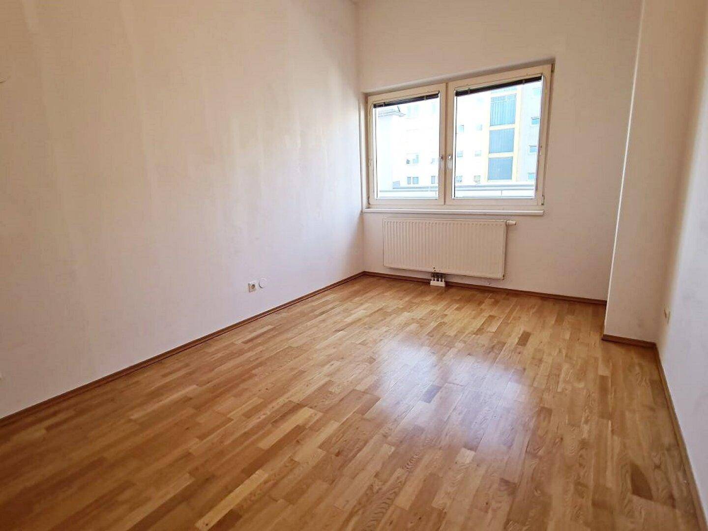 Helles Zimmer mit Parkettboden und großem Fenster, ideal für Schlaf- oder Arbeitszimmer.