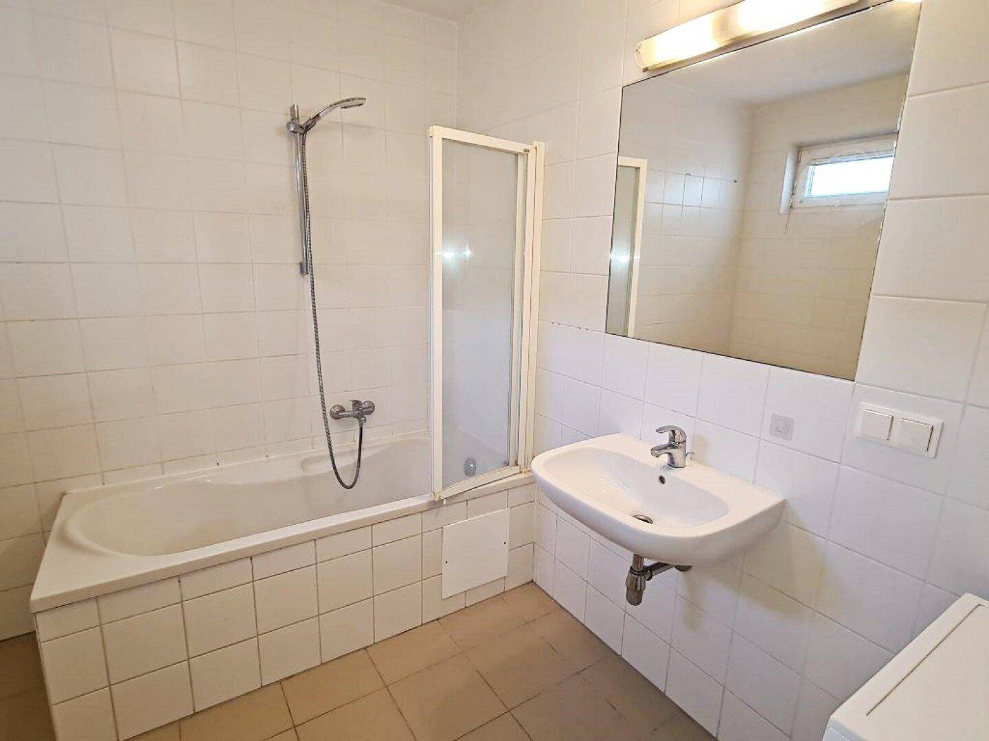 Helles Badezimmer mit Badewanne, Duschabtrennung und Waschbecken, gefliest in Weiß und Beige.