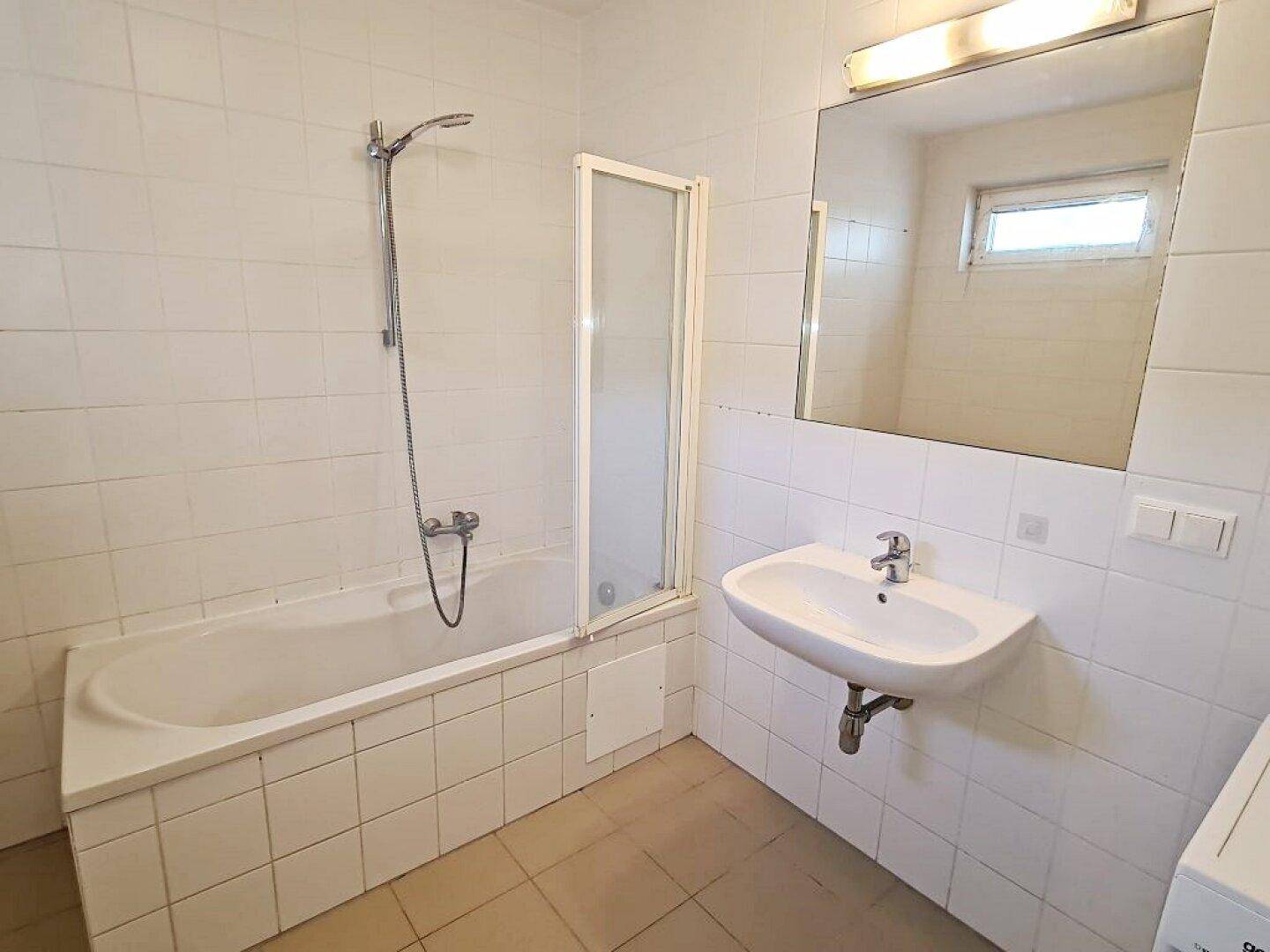 Funktionales Badezimmer mit Badewanne, Duschvorrichtung und Waschbecken, hell gefliest.