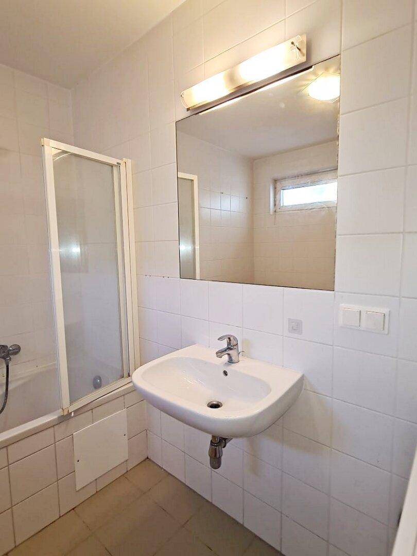 Badezimmer mit Waschbecken, großem Spiegel und Fenster, ausgestattet mit weißen Fliesen.