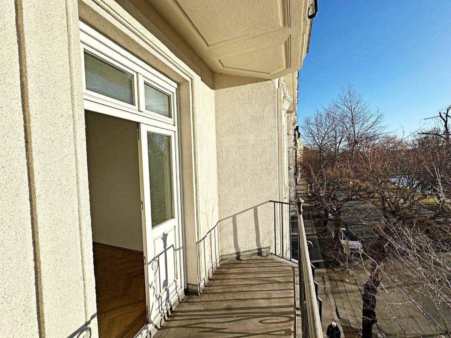 Langer Balkon mit schmiedeeisernem Geländer und weitem Blick auf die Straße und Bäume.